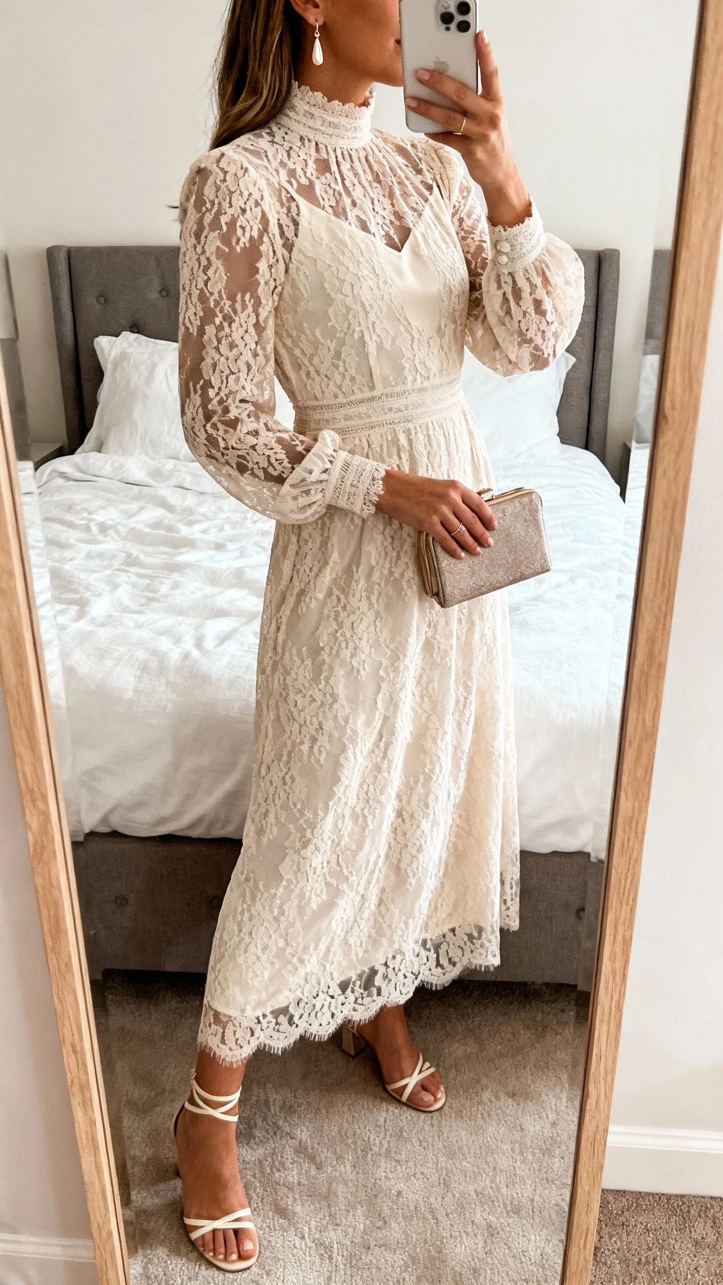 iPhone back/side mirror selfie of a woman in a lace-overlay high-neck dress with a modest lining, delicate drop earrings, strappy low heels, small clutch, face not visible, bedroom mirror, soft natural light, iPhone photo quality.
