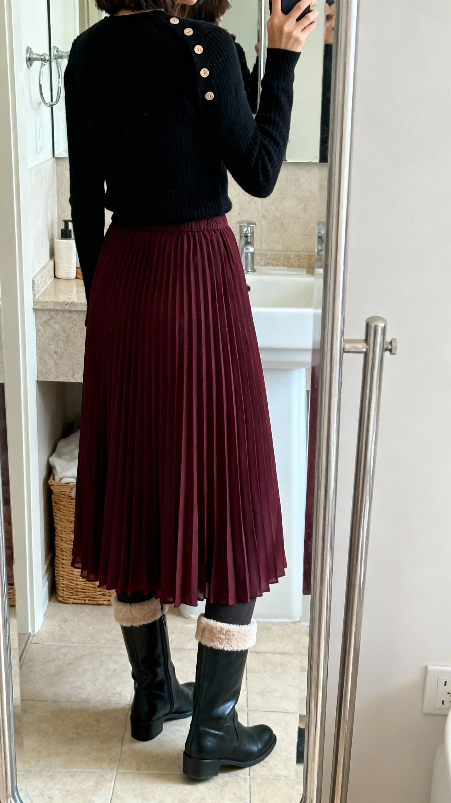 iPhone back-view mirror selfie of a woman wearing a deep burgundy pleated chiffon maxi skirt, fitted black crewneck sweater buttoned look, fleece-lined tights, and knee-high black boots, face not visible, bathroom full-length mirror with soft daylight, iPhone photo quality.