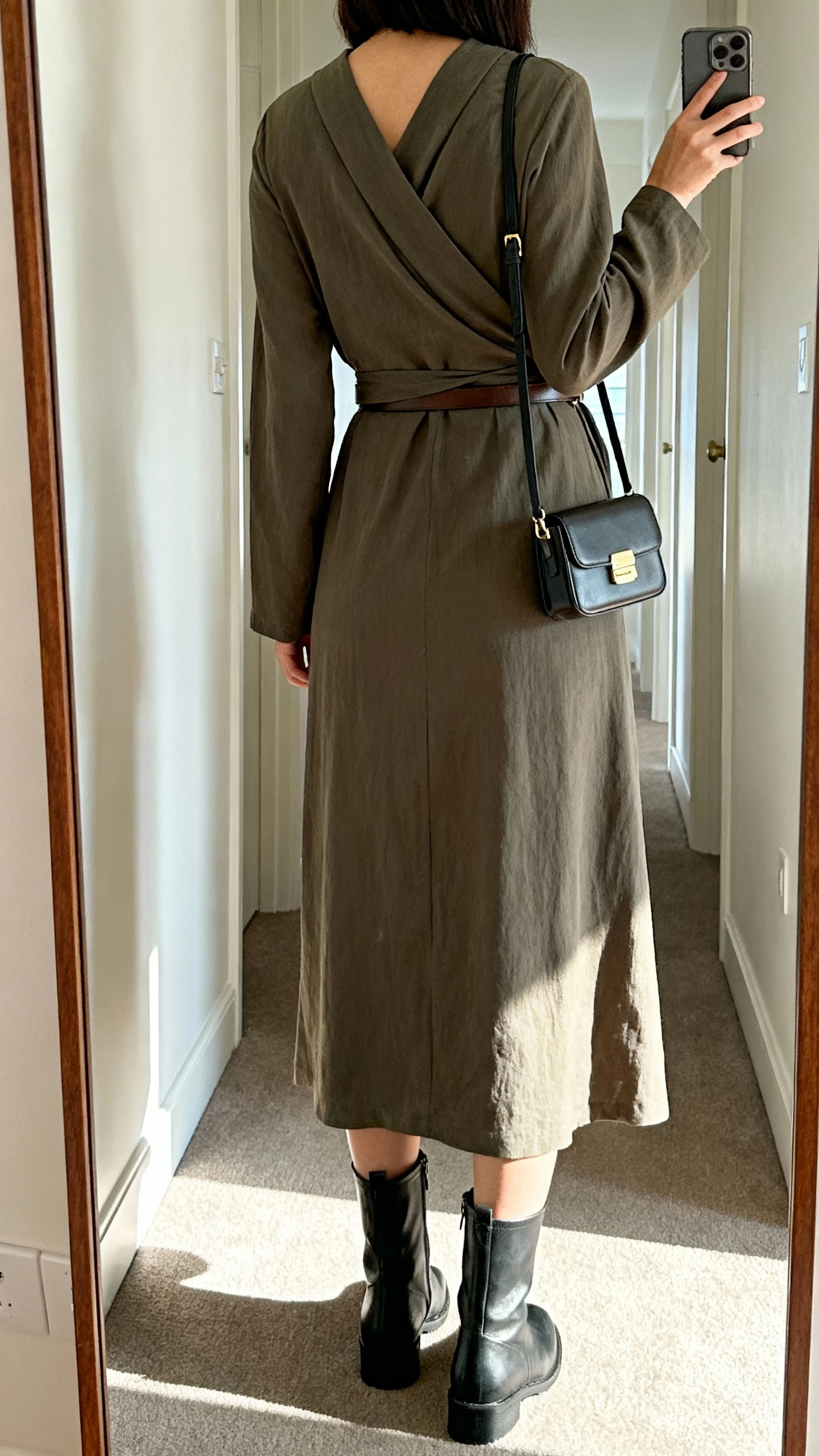 iPhone back view mirror selfie of a woman wearing a long-sleeve wrap-effect dress with mid-calf boots, simple belt if needed, and a compact crossbody, face not visible, full-length mirror in hallway, natural daylight, iPhone photo quality.