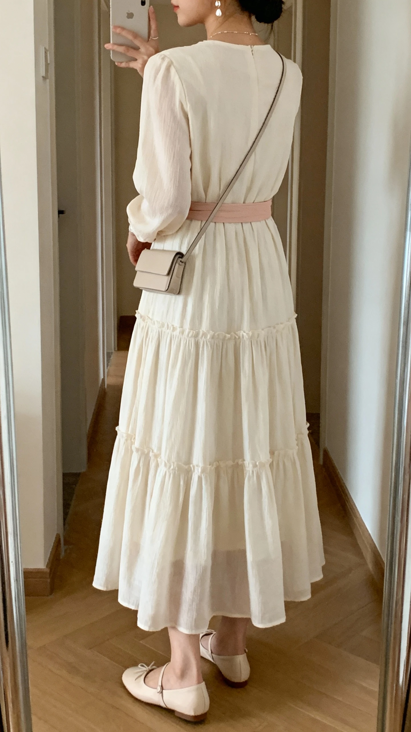iPhone back-view mirror selfie of a woman wearing a tiered maxi dress with a soft belt and ballet flats, delicate earrings and a slim crossbody, face not visible, hallway mirror, gentle indoor lighting, iPhone photo quality