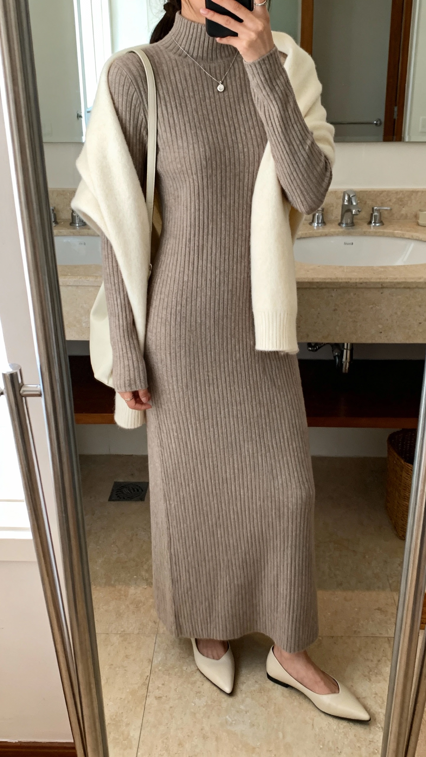 iPhone back-view mirror shot of a woman in a long-sleeve ribbed knit maxi dress (mock neck) with a cream cashmere shawl wrap draped over her shoulders, pointed-toe flats, a subtle pendant necklace under the neckline, and a soft shoulder bag; face not visible, bathroom mirror, natural indoor light, iPhone photo quality.