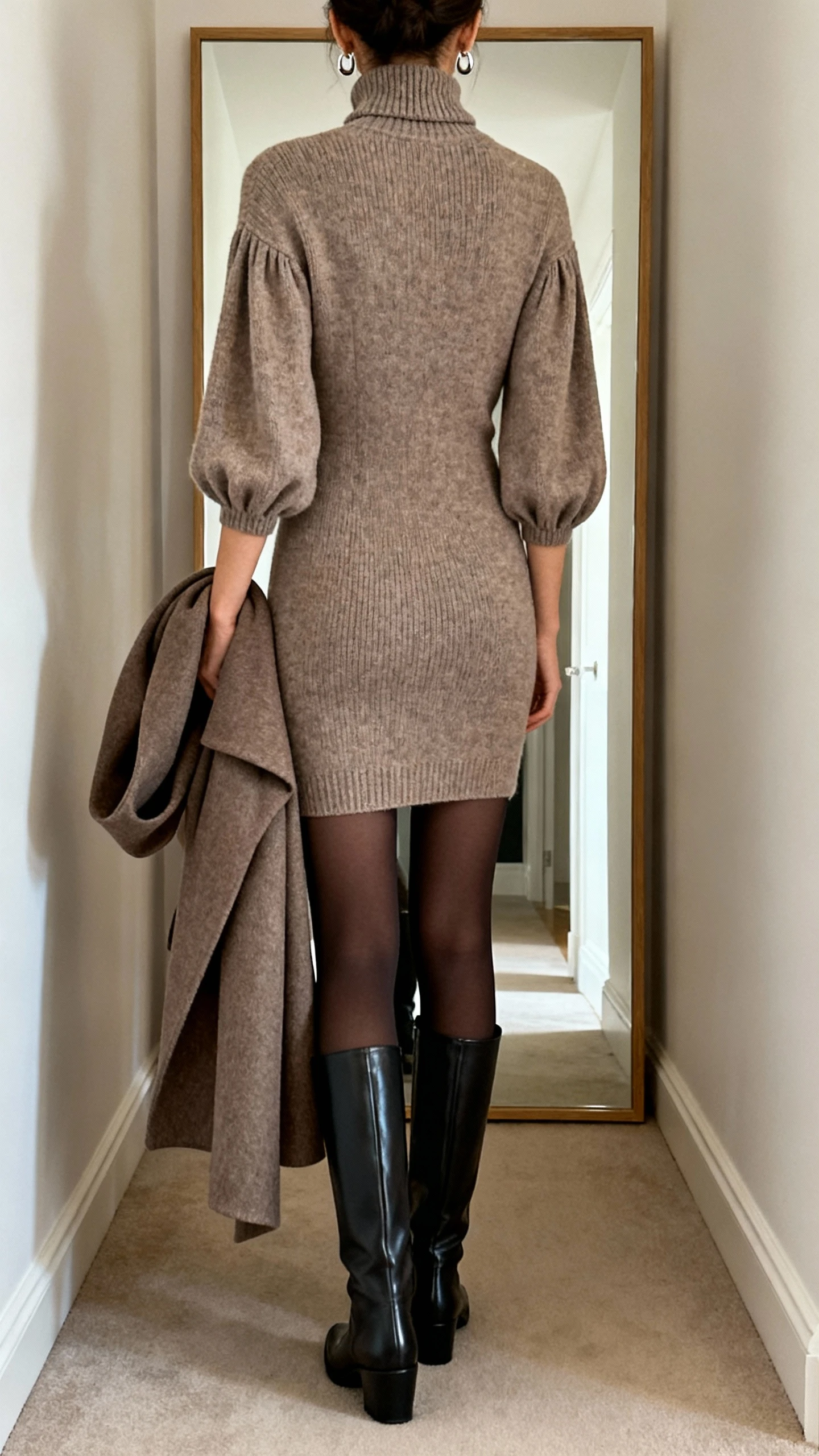 iPhone back-view mirror shot of a woman wearing a knit sheath dress with bishop sleeves and a mock neck, matte opaque black or espresso tights, sleek knee-high or ankle boots, minimal drop earrings, and a structured wool or wrap coat draped over her arm; face not visible, hallway full-length mirror, indoor lighting, iPhone photo quality.
