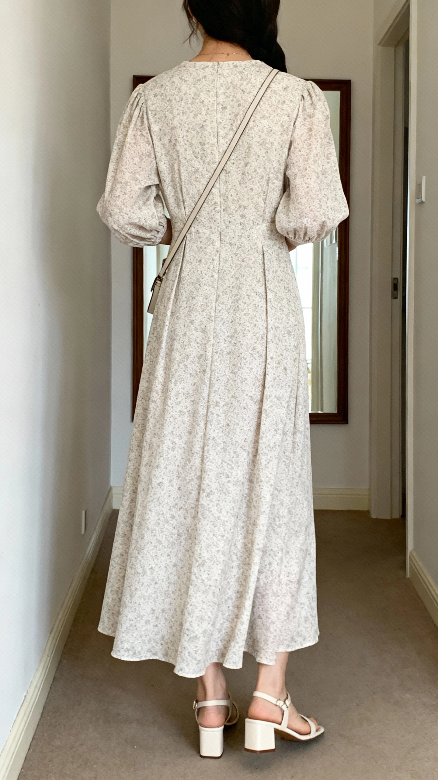 iPhone back view of a woman wearing a refined maxi dress with sleeves and a subtle print, styled with simple block-heel sandals and a slim crossbody, face not visible, hallway mirror, natural daylight, iPhone photo quality.
