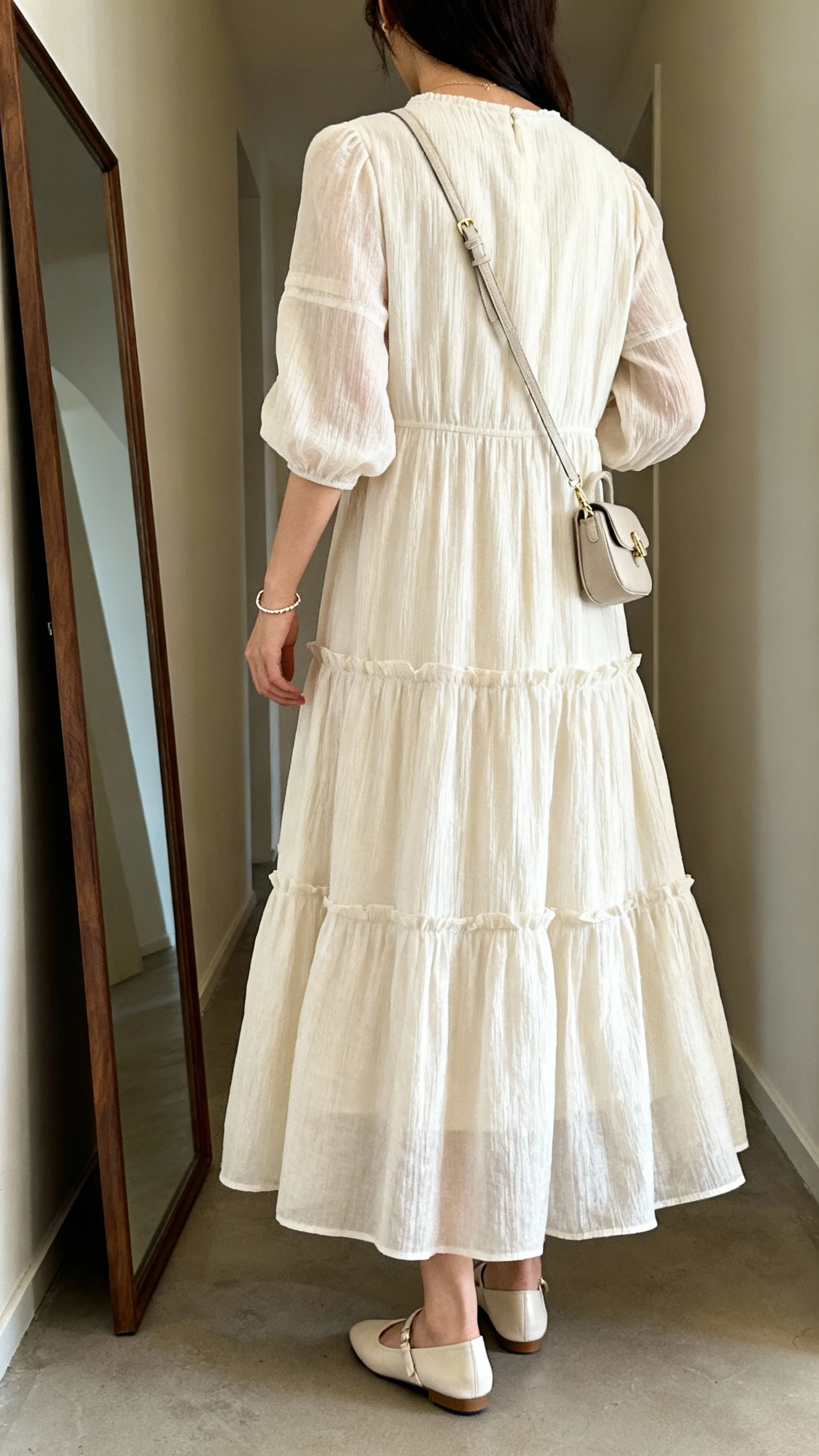 iPhone back view of a woman wearing a tiered maxi dress with refined flats, delicate bracelet, and a small crossbody, face not visible, hallway full-length mirror, natural daylight, iPhone photo quality.