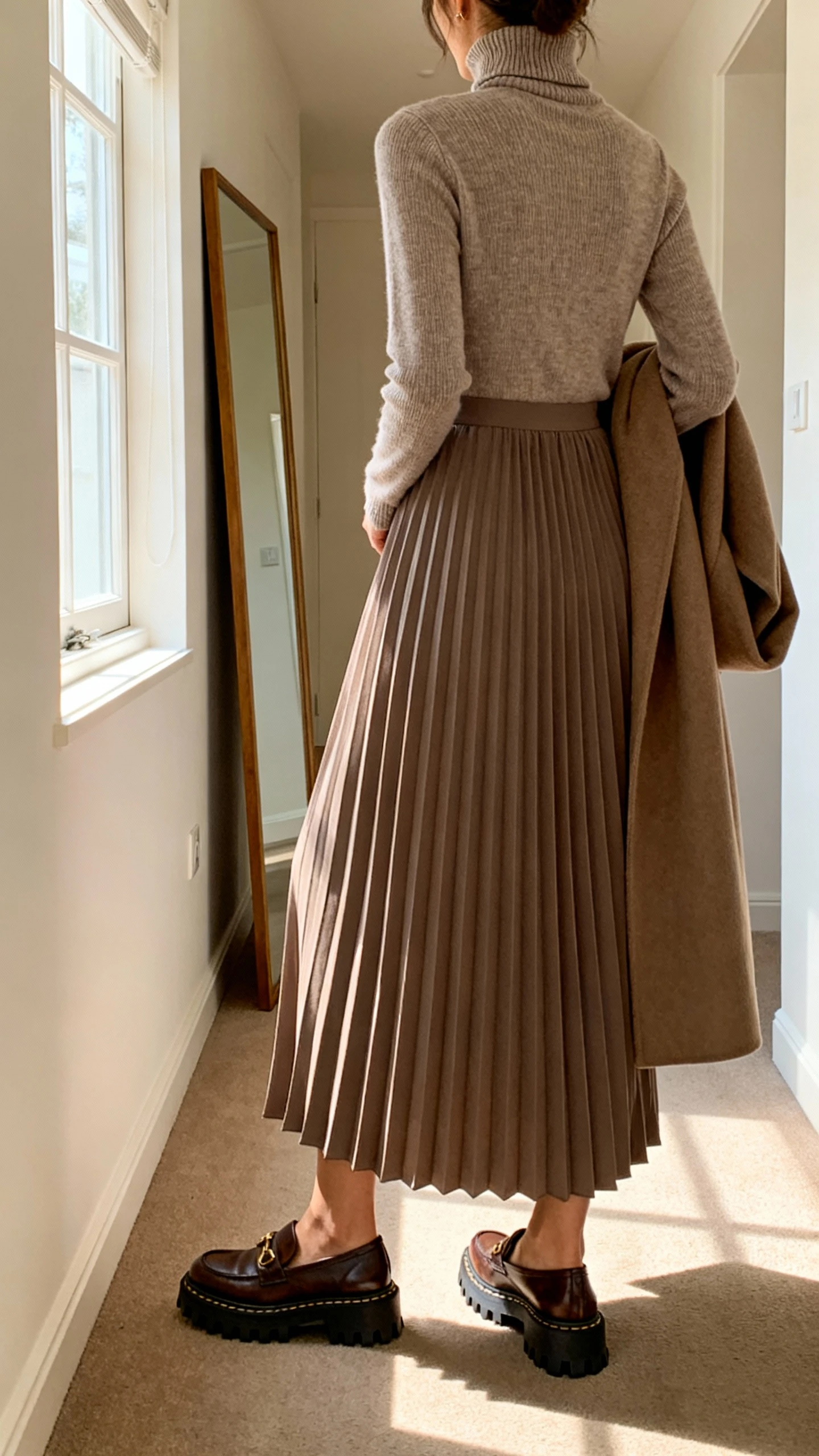iPhone back view of a woman wearing a turtleneck pleated maxi dress with lug-sole loafers and a longline coat draped over, face not visible, hallway mirror, morning light from a window, iPhone photo quality.