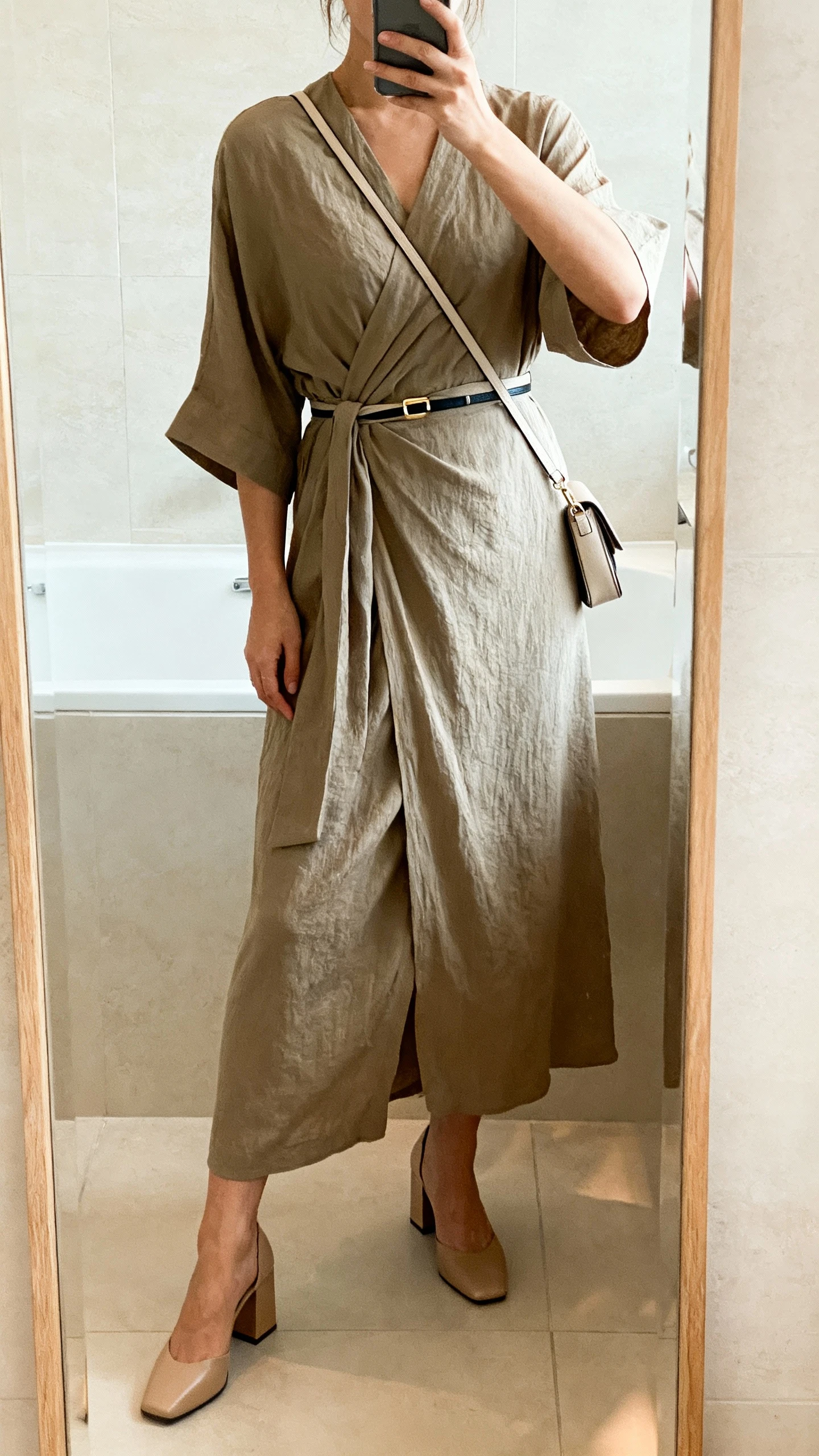 iPhone mirror selfie of a woman in a wrap-style maxi dress with block heels and a slim belt, carrying a simple crossbody, face not visible, bathroom mirror, soft indoor lighting, iPhone photo quality