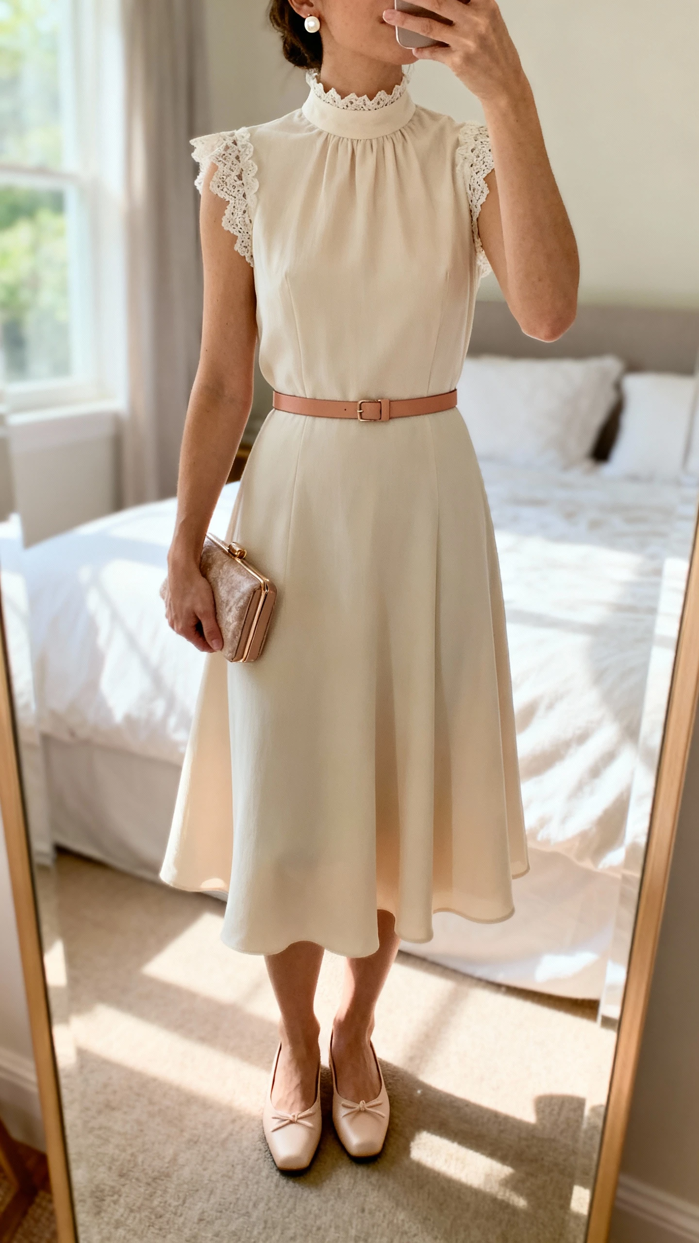 iPhone mirror selfie of a woman in an A-line dress with a high neckline and soft lace trim, thin waist-defining satin or leather belt, classic ballet flats or low block heels, small pearl or crystal stud earrings, and a compact clutch; face not visible, cropped at shoulders, bedroom mirror, natural daylight, iPhone photo quality.