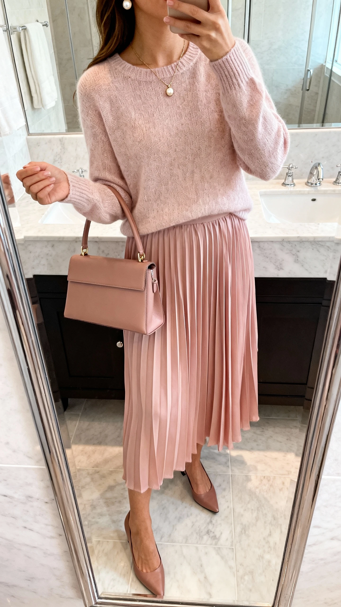 iPhone mirror selfie of a woman wearing a blush pleated chiffon skirt, fine-gauge crewneck sweater, low-heel slingbacks, structured top-handle bag, dainty pendant necklace, and pearl earrings, face not visible, cropped at shoulders in a bathroom mirror, soft natural daylight, iPhone photo quality.