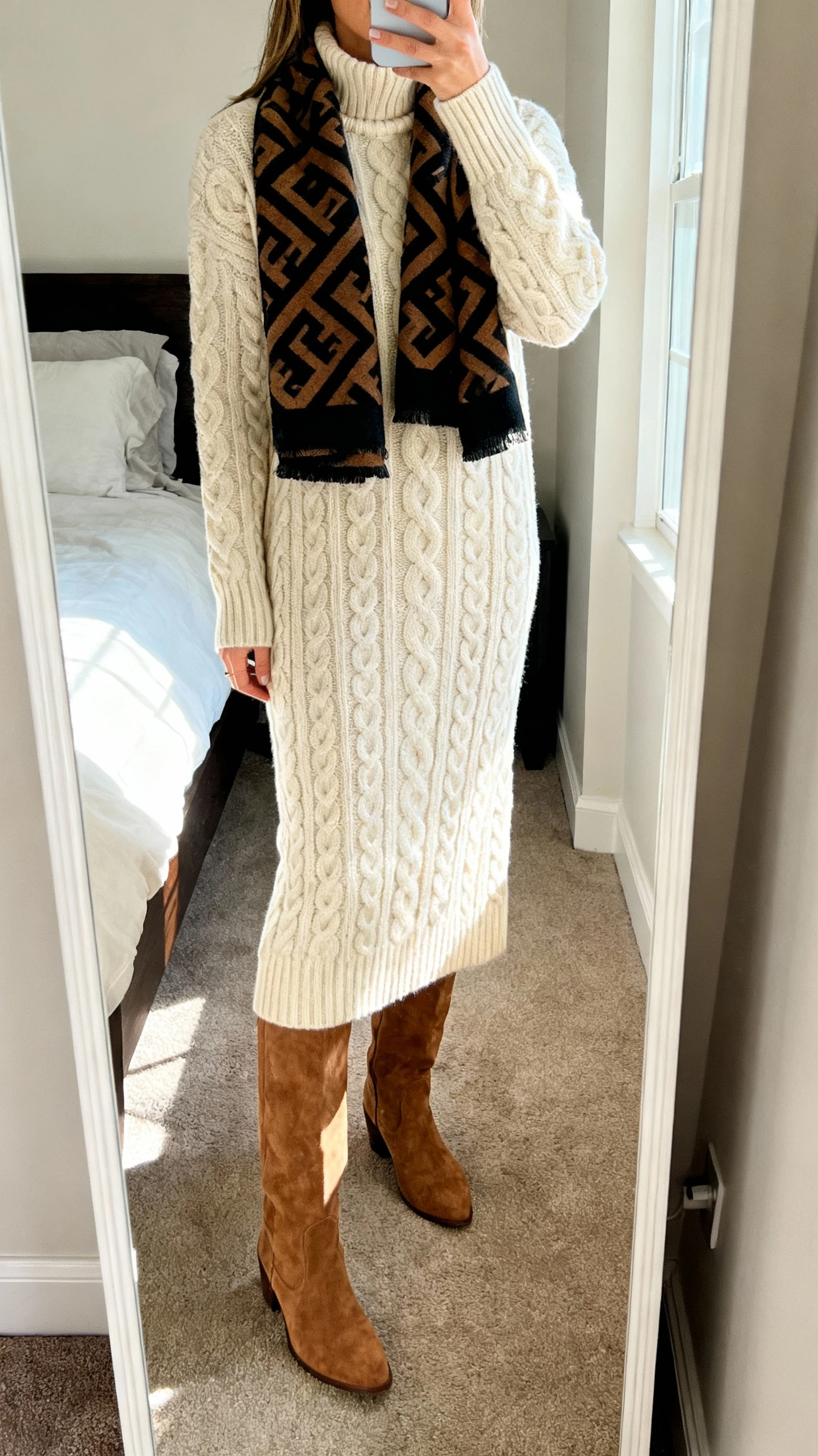 iPhone mirror selfie of a woman wearing a cable-knit mock-neck maxi dress with knee-high suede boots and a bold statement scarf, face not visible, cropped at shoulders, bedroom mirror, natural daylight, iPhone photo quality.