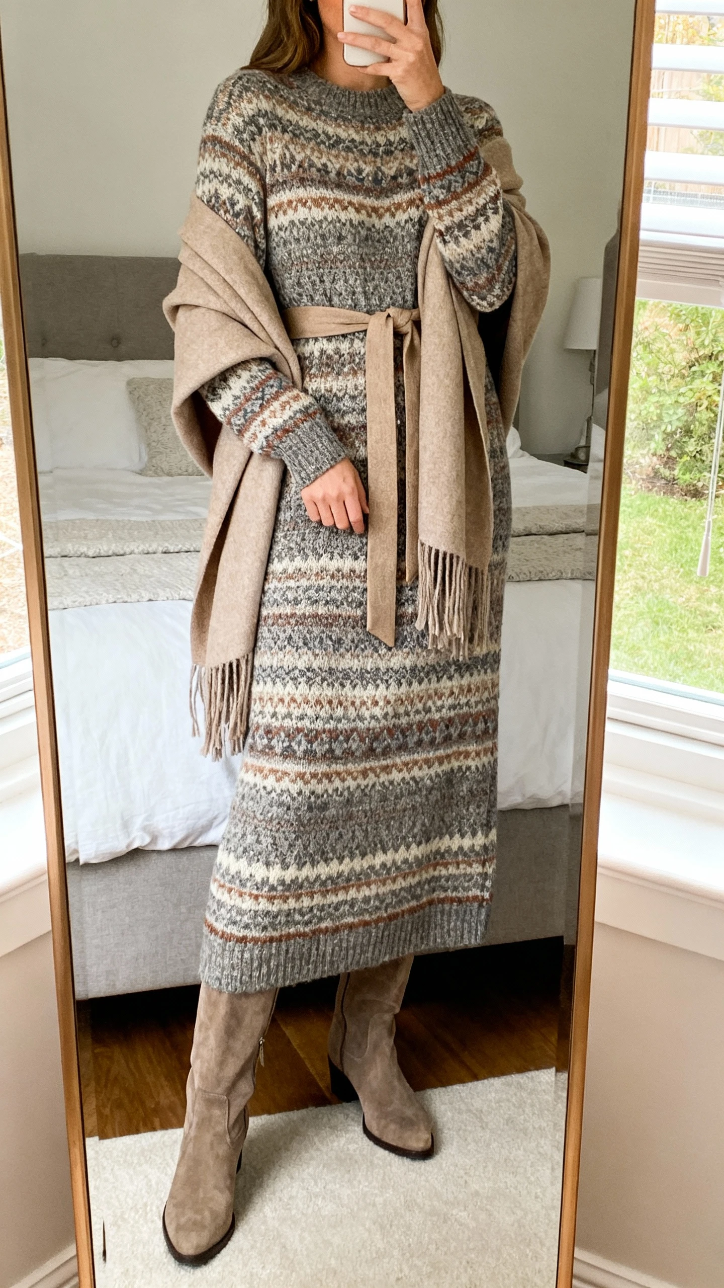 iPhone mirror selfie of a woman wearing a heritage knit maxi dress with tall boots and a belted wrap layered over, face not visible, cropped at neck, bedroom mirror, natural window light, iPhone photo quality.