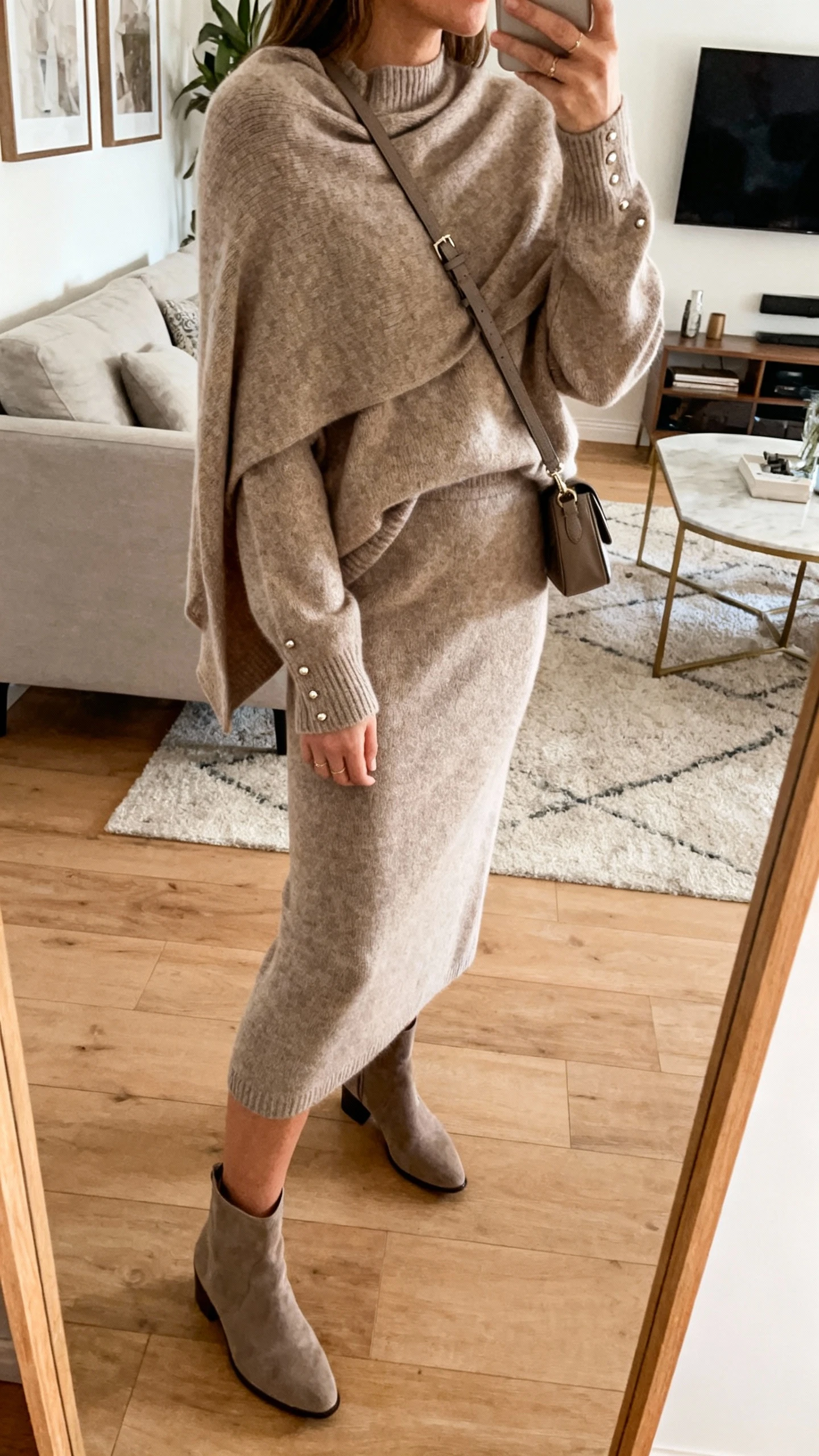 iPhone mirror selfie of a woman wearing a knit midi set (soft draped sweater and matching midi skirt) with zero cling, ankle boots, a crossbody bag, and minimal studs, face not visible, side angle, living room mirror, warm indoor lighting, iPhone photo quality.