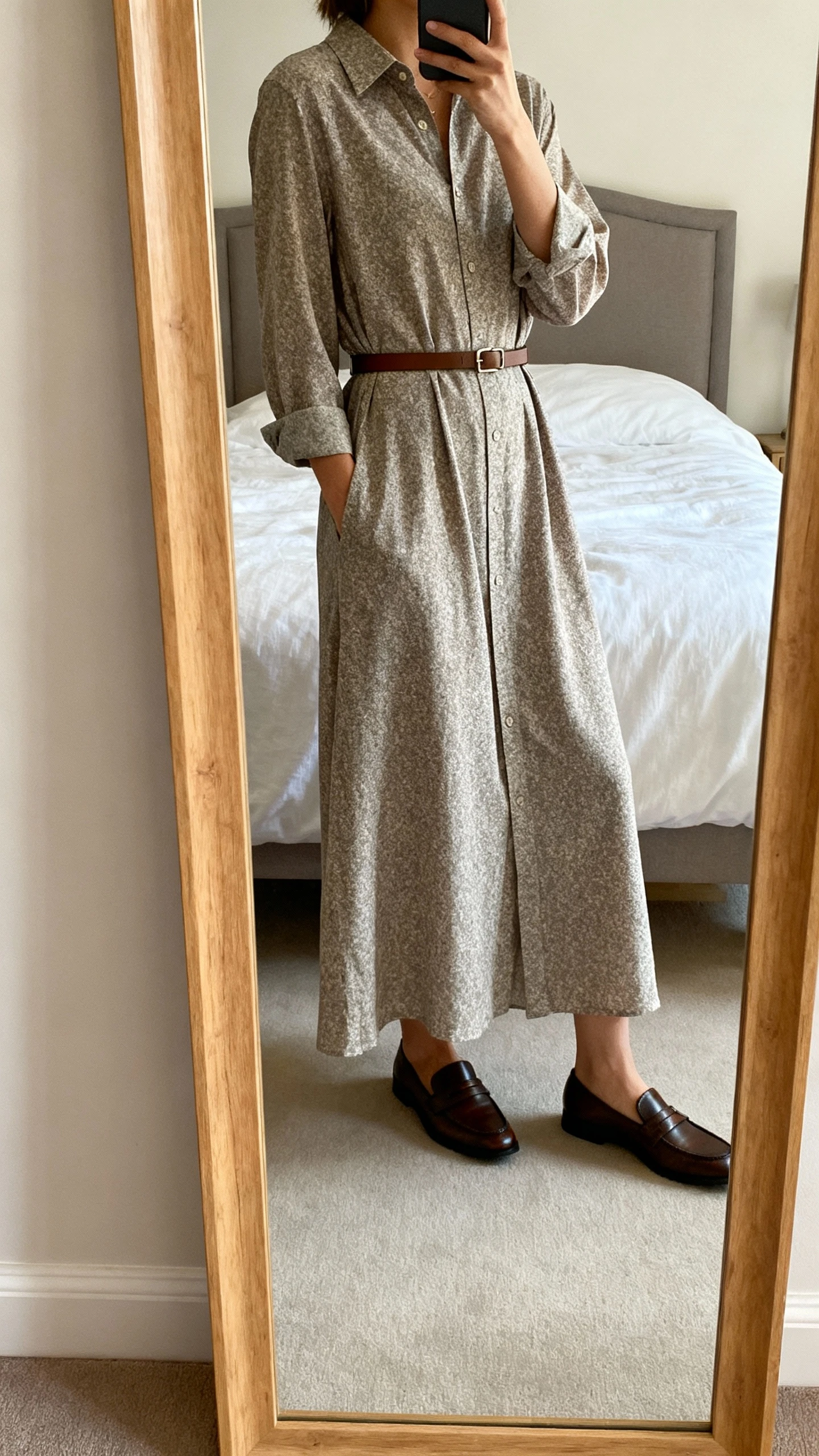 iPhone mirror selfie of a woman wearing a maxi shirt dress with a belted waist and a quiet pattern, classic loafers and a slim belt, face not visible, cropped at shoulders, bedroom mirror, natural daylight, iPhone photo quality