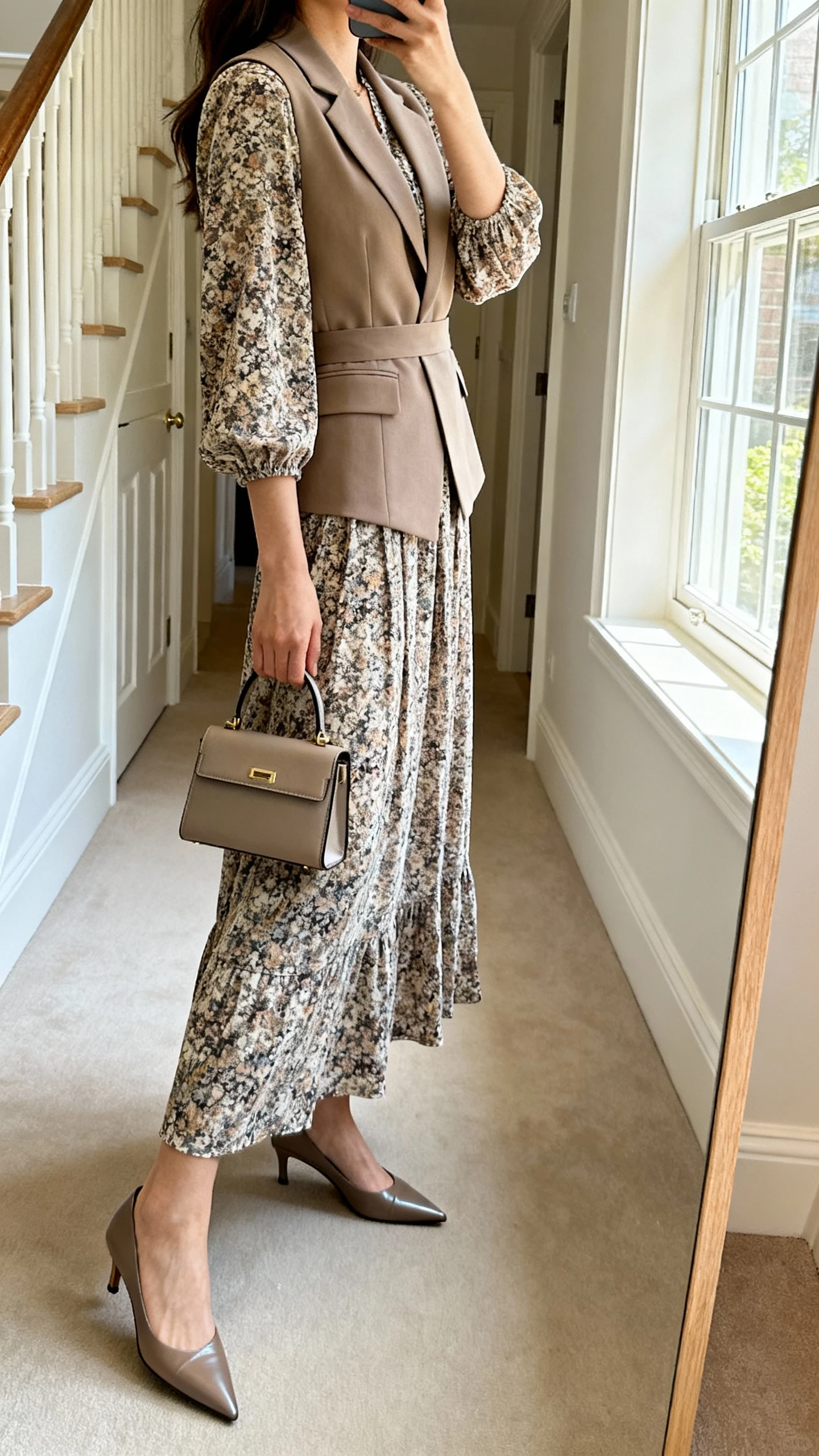 iPhone mirror selfie of a woman wearing a printed maxi dress with a tailored waistcoat and pointed-toe pumps, small structured handbag, face not visible, side angle, entryway mirror, soft window light, iPhone photo quality