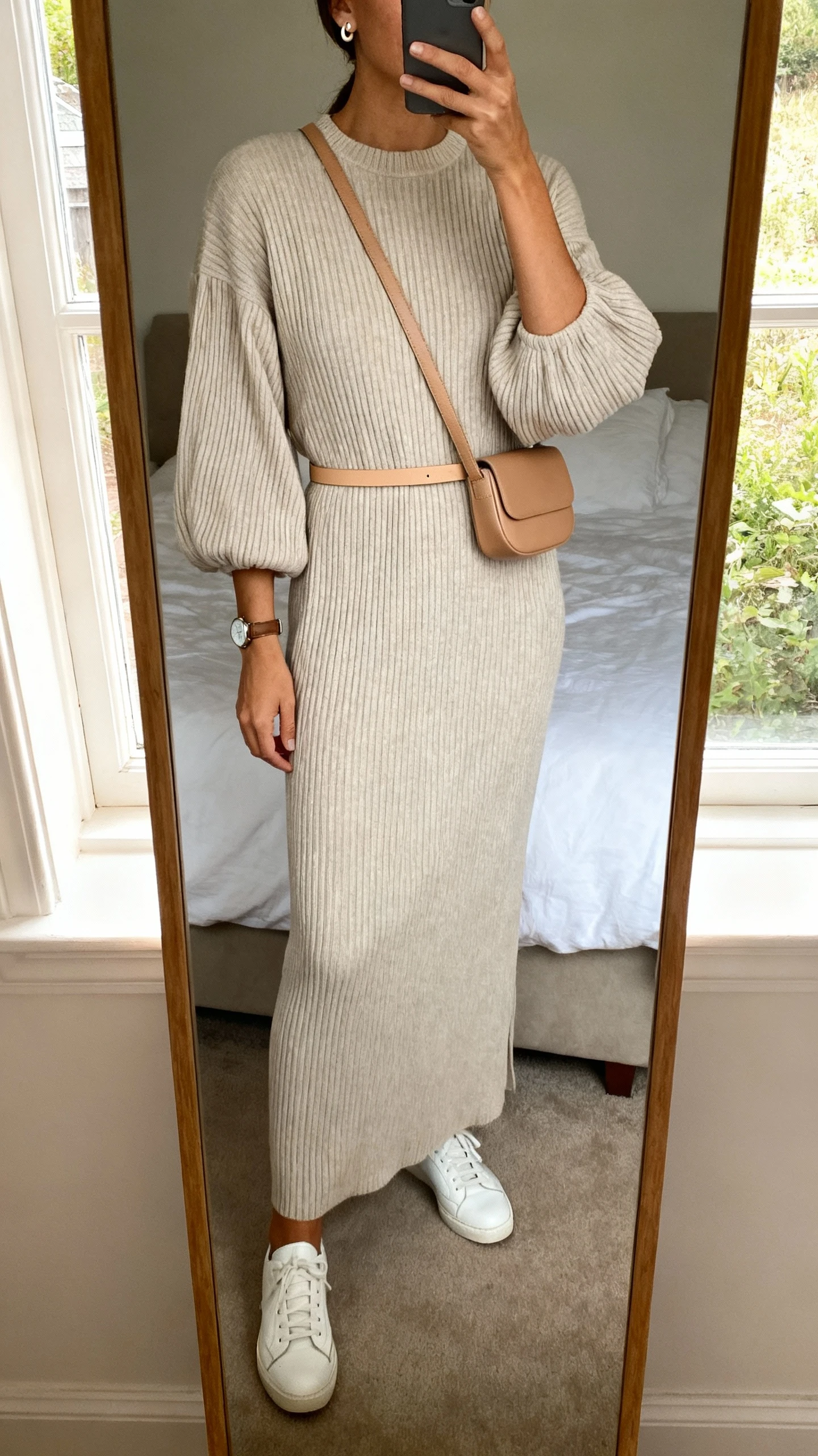 iPhone mirror selfie of a woman wearing a ribbed knit maxi dress with balloon sleeves and a crew neckline, white leather sneakers, a minimalist tan crossbody, a thin matching waist belt, stud earrings, and a simple watch; face not visible, cropped at shoulders, bedroom mirror, soft afternoon window light, iPhone photo quality.