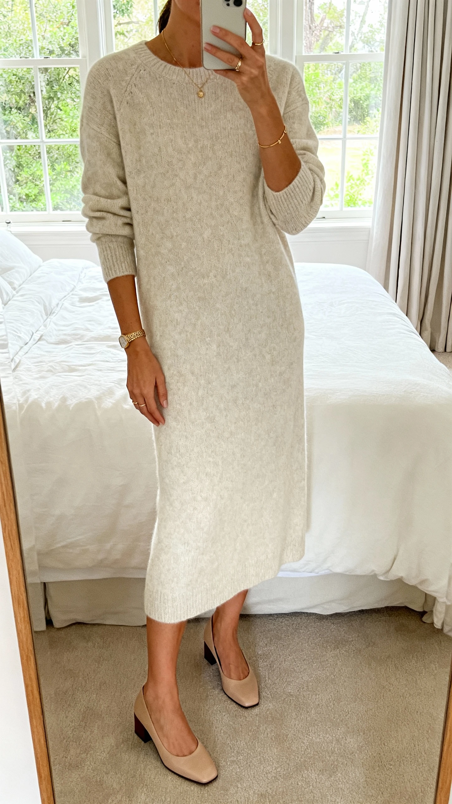iPhone mirror selfie of a woman wearing a soft midi sweater dress with quiet-luxury polish, minimal jewelry and low block heels, face not visible, cropped at neck, bedroom mirror with natural window light, iPhone photo quality