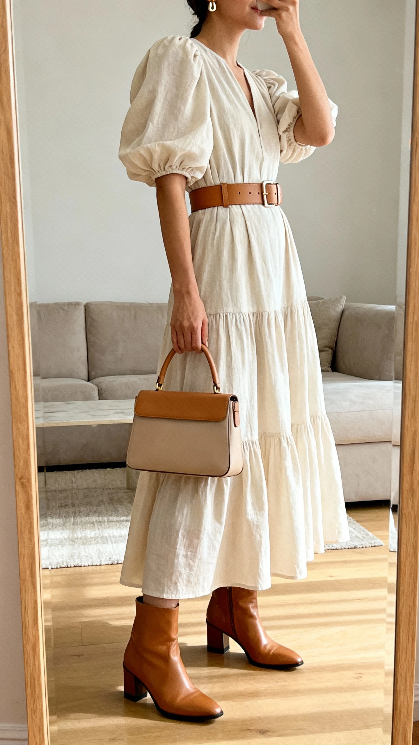 iPhone mirror selfie of a woman wearing a tiered maxi dress with puff sleeves, a camel leather waist belt, leather ankle boots with a low heel, a structured top-handle bag, and small-scale statement earrings; face not visible, side angle, living room full-length mirror, natural morning light, iPhone photo quality.