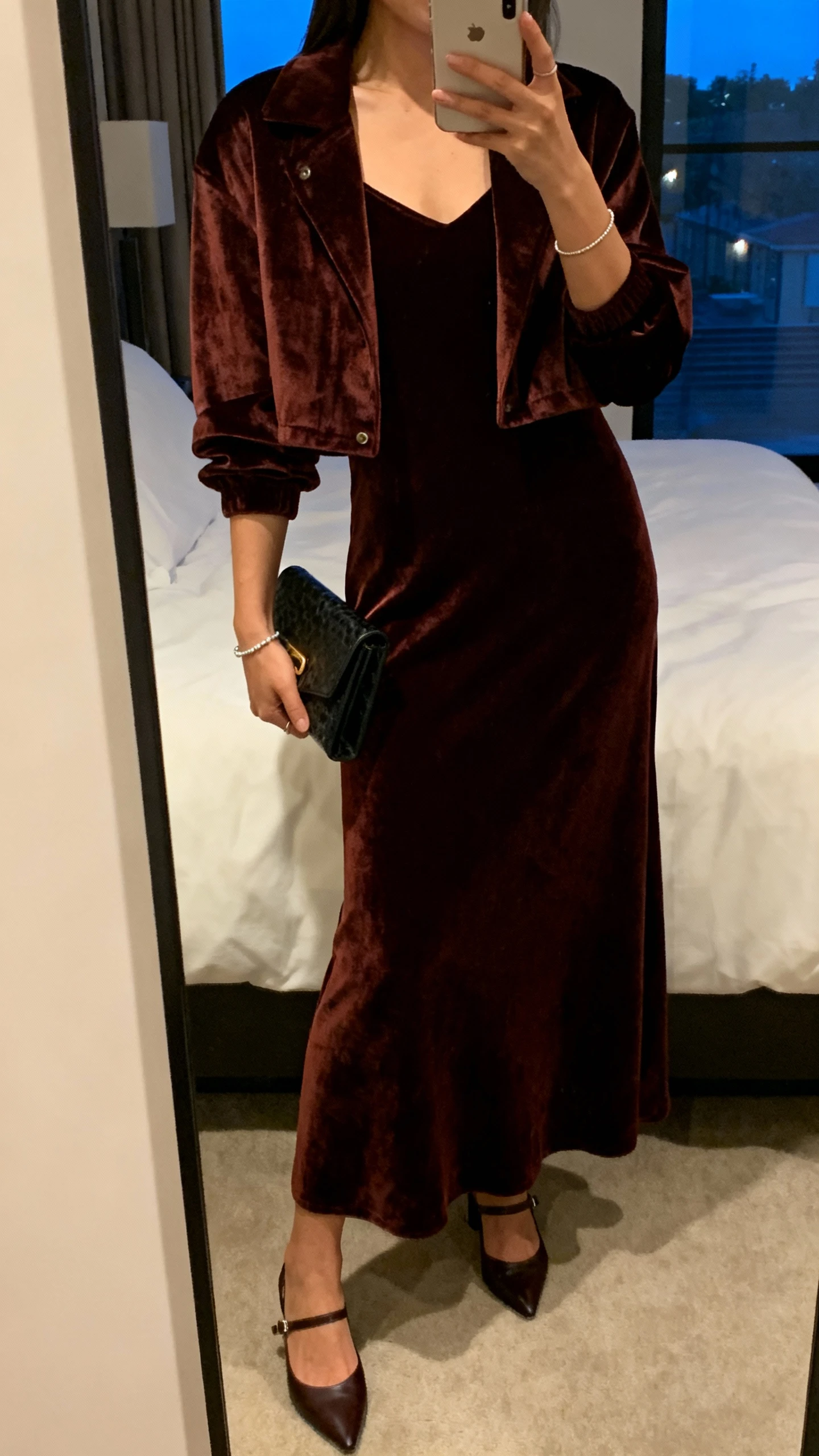 iPhone mirror selfie of a woman wearing a velvet maxi dress with a cropped jacket and slingback heels, clutch bag and subtle bracelet, face not visible, cropped at neck, bedroom mirror, evening indoor lighting, iPhone photo quality
