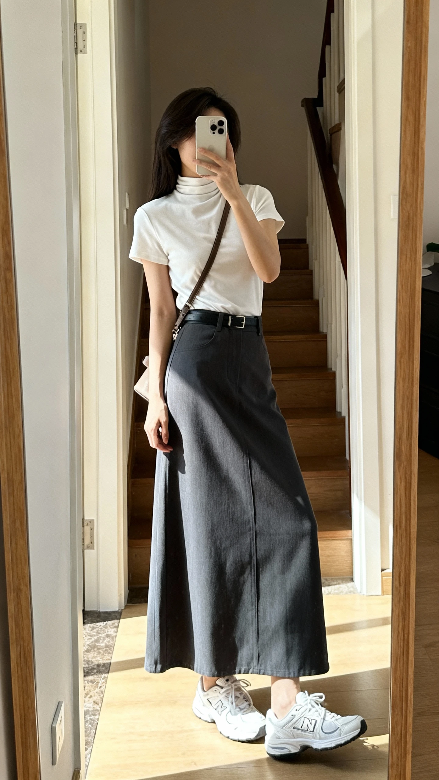 iPhone mirror selfie of a woman wearing an elevated high-neck tee tucked into a maxi skirt with clean white sneakers and a crossbody bag, face not visible, side angle, entryway full-length mirror, bright natural daylight, iPhone photo quality