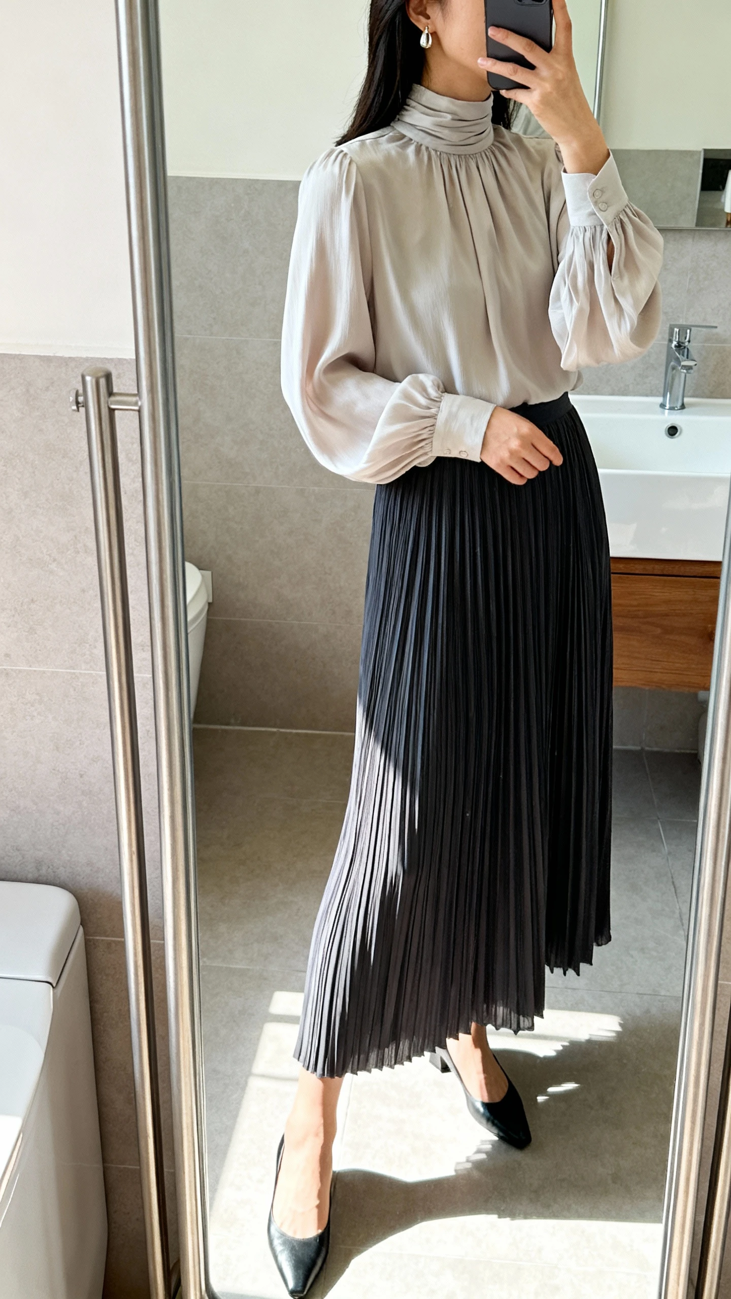 iPhone side-angle mirror selfie of a woman wearing a pleated midi skirt and a high-neck blouse with graceful movement, delicate earrings, low pumps, face not visible, bathroom full-length mirror, morning indoor light, iPhone photo quality