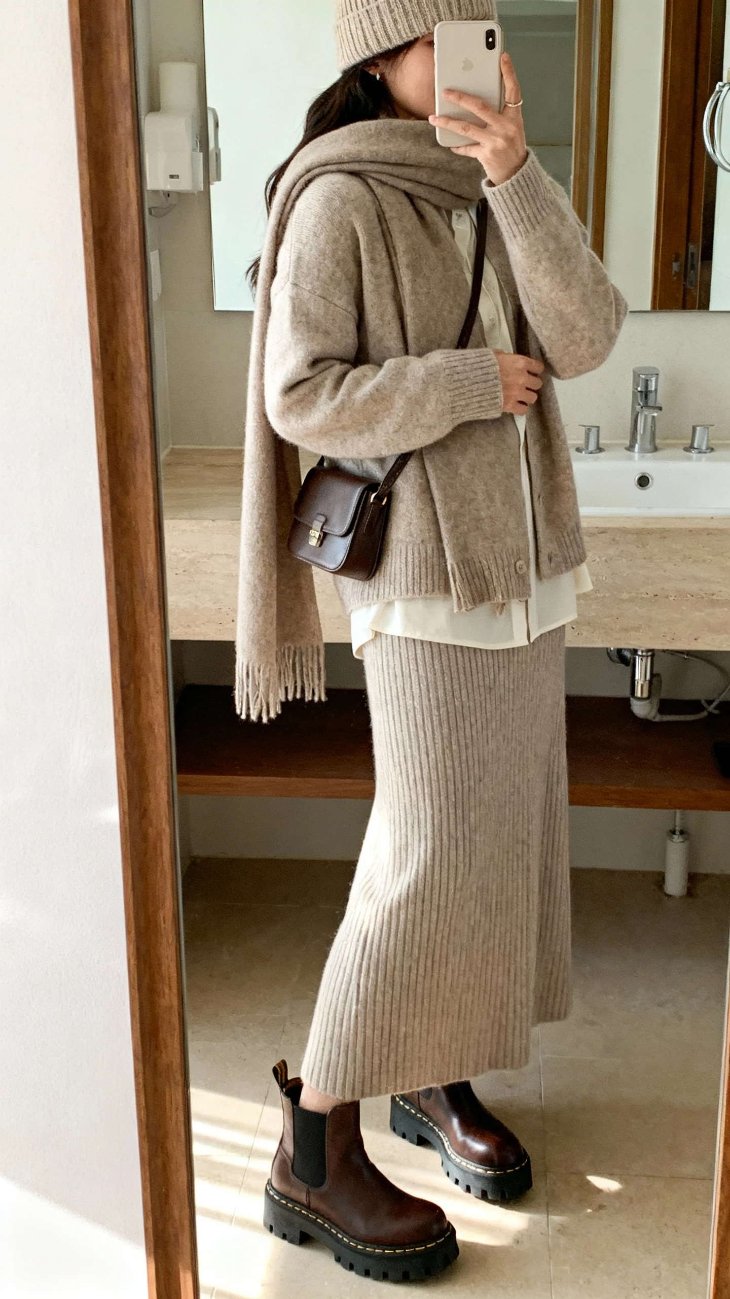 iPhone side-angle mirror selfie of a woman wearing a cozy ribbed knit maxi dress with tonal layered cardigan and long scarf, lug-sole Chelsea boots, crossbody bag, and knit beanie, face not visible, cropped at shoulders, bathroom mirror, soft natural light, iPhone photo quality.