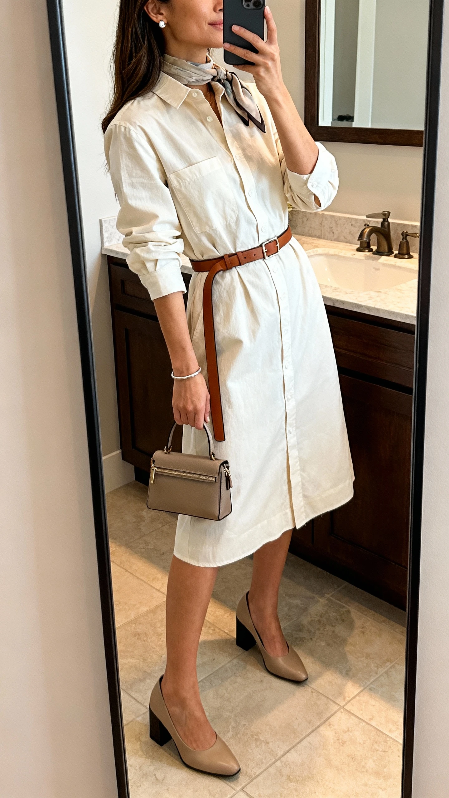 iPhone side-angle mirror selfie of a woman wearing a cotton poplin midi shirt dress with a self belt and an added slim leather belt, closed-toe block heels, a structured mini bag, stud earrings, a simple bangle, and a subtle scarf; face not visible, bathroom mirror, indoor lighting, iPhone photo quality.