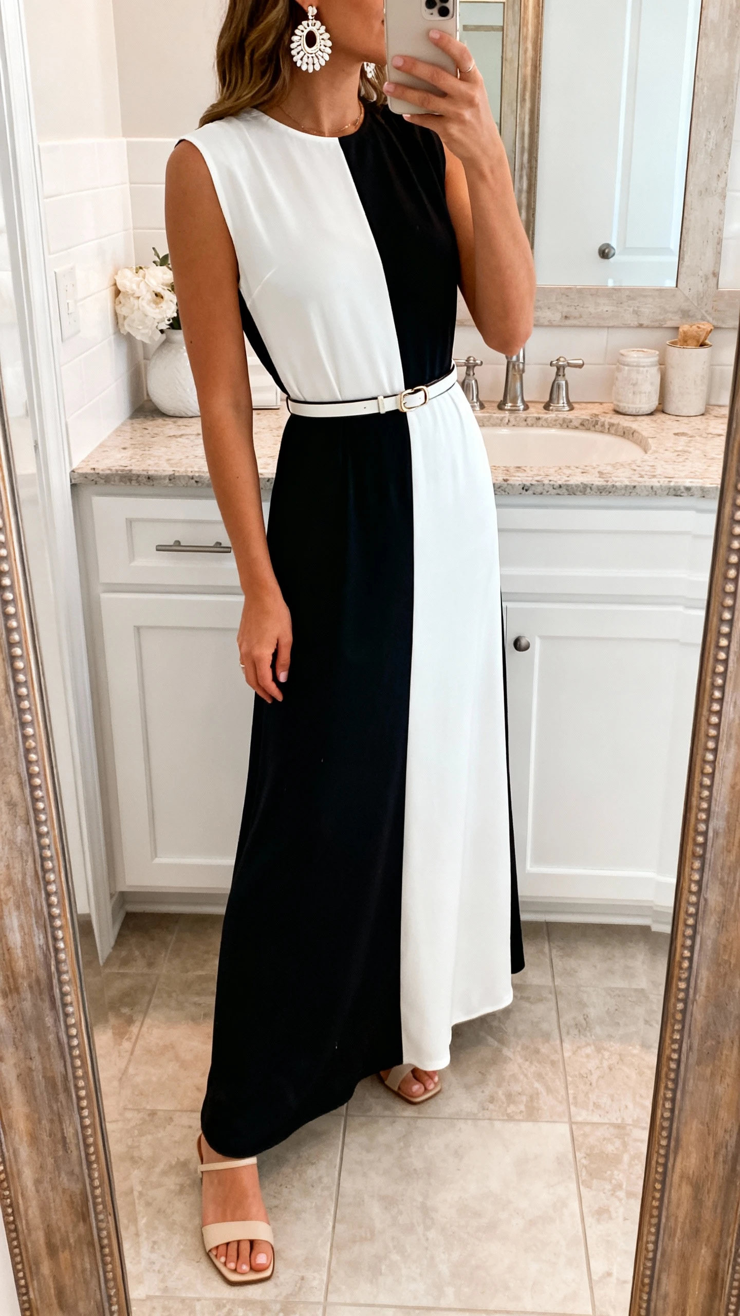 iPhone side-angle mirror selfie of a woman wearing a monochrome maxi dress with statement earrings, slim belt, and minimal heeled sandals, face not visible, bathroom mirror, bright indoor lighting, iPhone photo quality