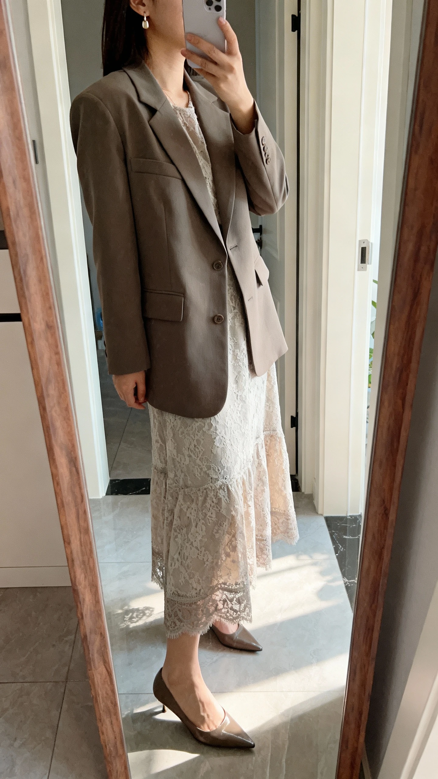 iPhone side-angle mirror selfie of a woman wearing a lace-trim maxi dress with a structured suit jacket, dainty earrings, and pointed-toe pumps, face not visible, entryway full-length mirror, morning natural light, iPhone photo quality