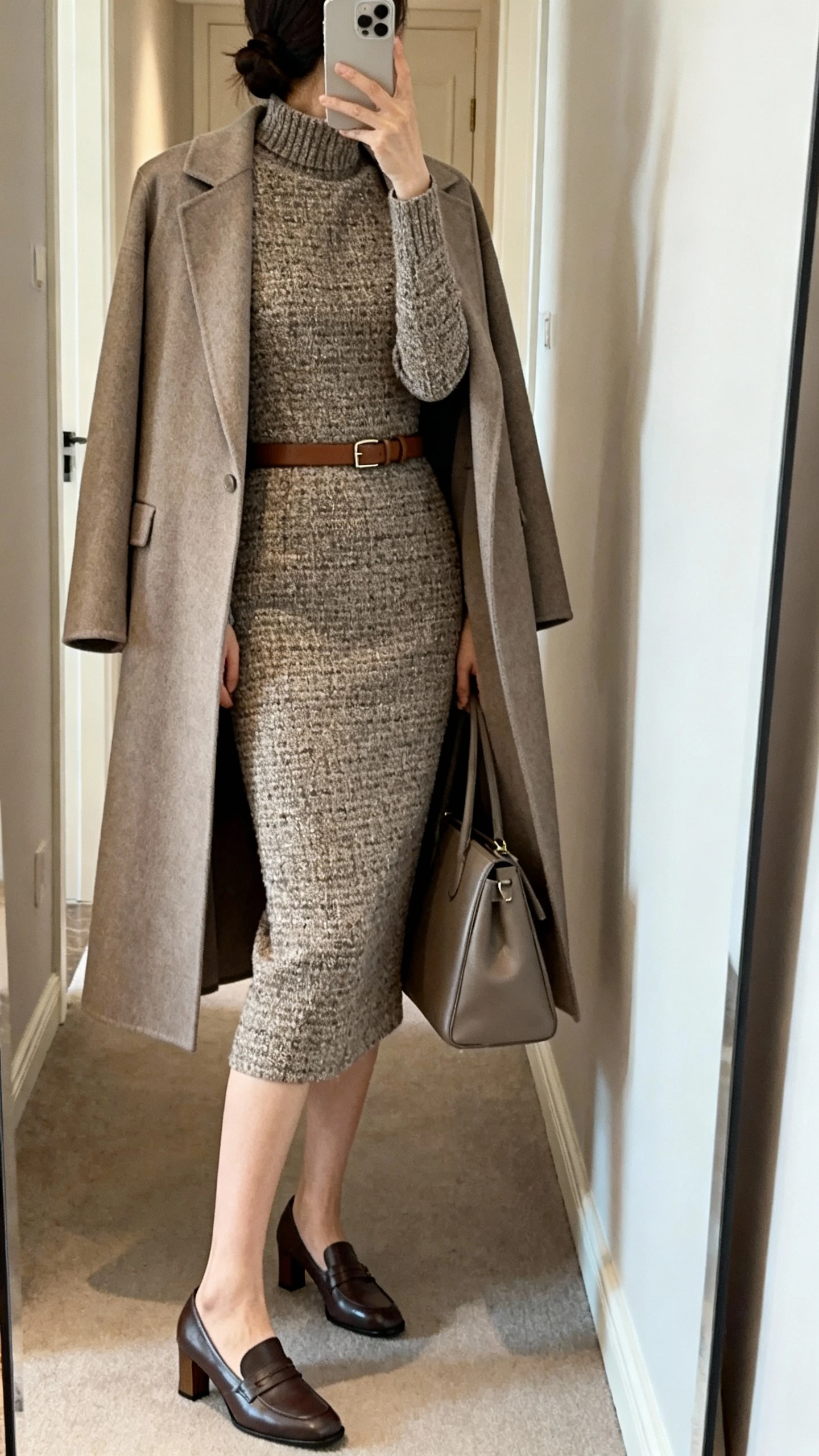 iPhone back-view mirror selfie of a woman wearing a tweed sheath dress with a high neckline and below-the-knee length, a collarless long coat in stone, heeled loafers, a slim leather belt under the coat, and carrying a medium structured tote; face not visible, hallway full-length mirror, soft indoor lighting, iPhone photo quality.