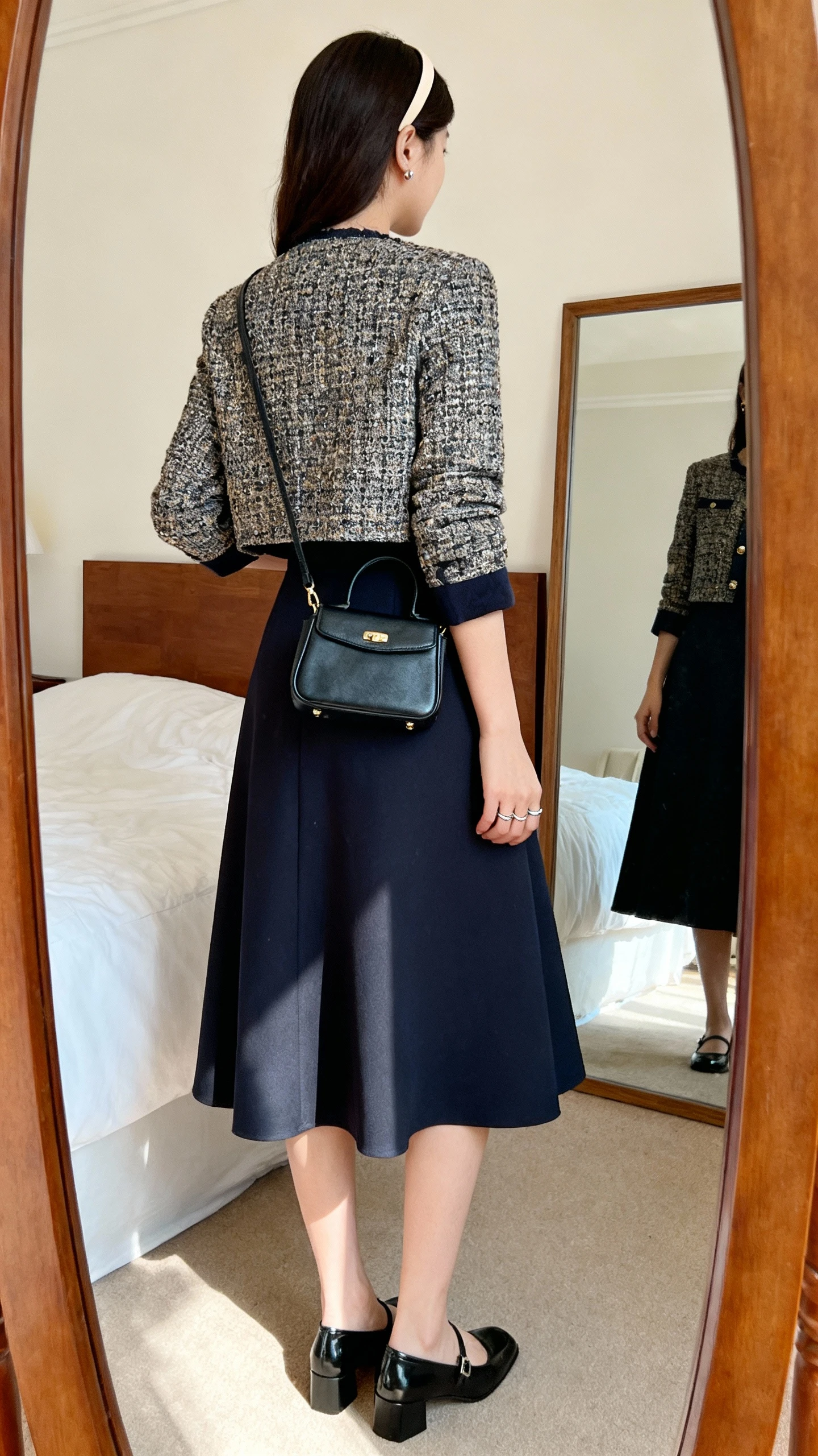 iPhone back view of a woman in a fit-and-flare midi dress with elbow-length sleeves, low block-heel Mary Janes, cropped tweed jacket, small structured mini satchel, thin headband, simple ring and studs, face not visible, bedroom mirror, natural daylight, iPhone photo quality.