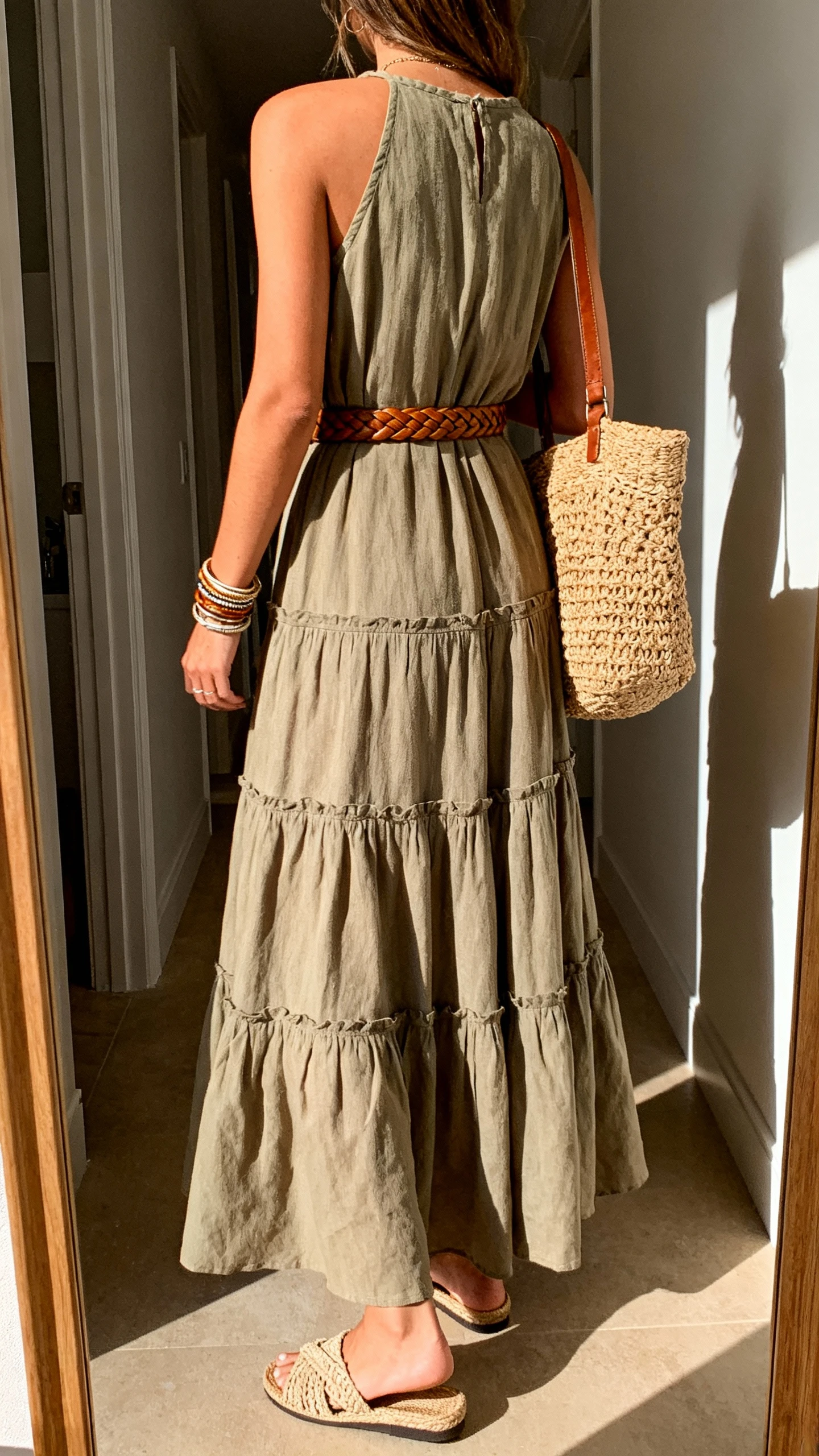 iPhone back view of a woman wearing a boho-polished tiered maxi dress in earthy tones, braided leather belt, textured straw tote, layered bangles, and woven slide sandals, face not visible, casual hallway mirror, late-afternoon daylight, iPhone photo quality