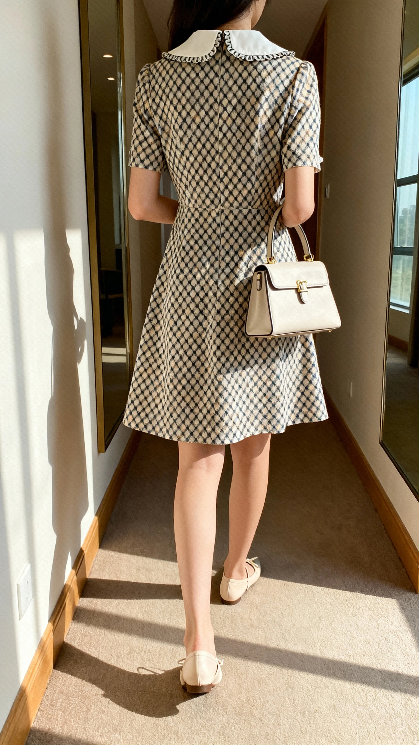 iPhone back view of a woman wearing a diamond-print A-line dress with a pretty collar detail, styled with a small structured top-handle bag and ballet flats, face not visible, hallway mirror, gentle daylight from window, iPhone photo quality.