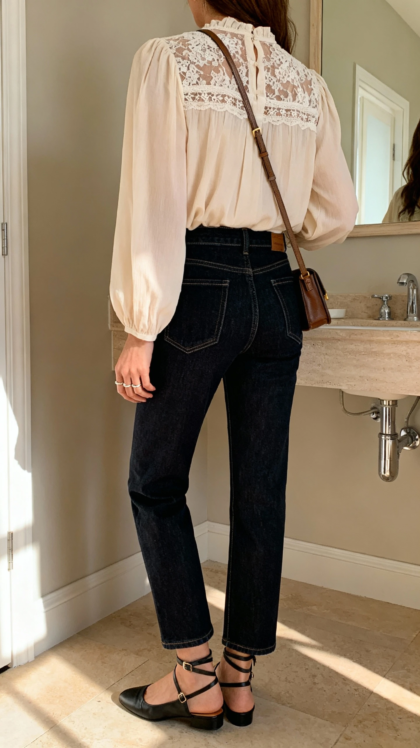 iPhone back view of a woman wearing a romantic lace-inset blouse with polished dark-wash denim, ankle-strap flats, a crossbody bag, and dainty rings, face not visible, casual bathroom mirror, soft afternoon light, iPhone photo quality.