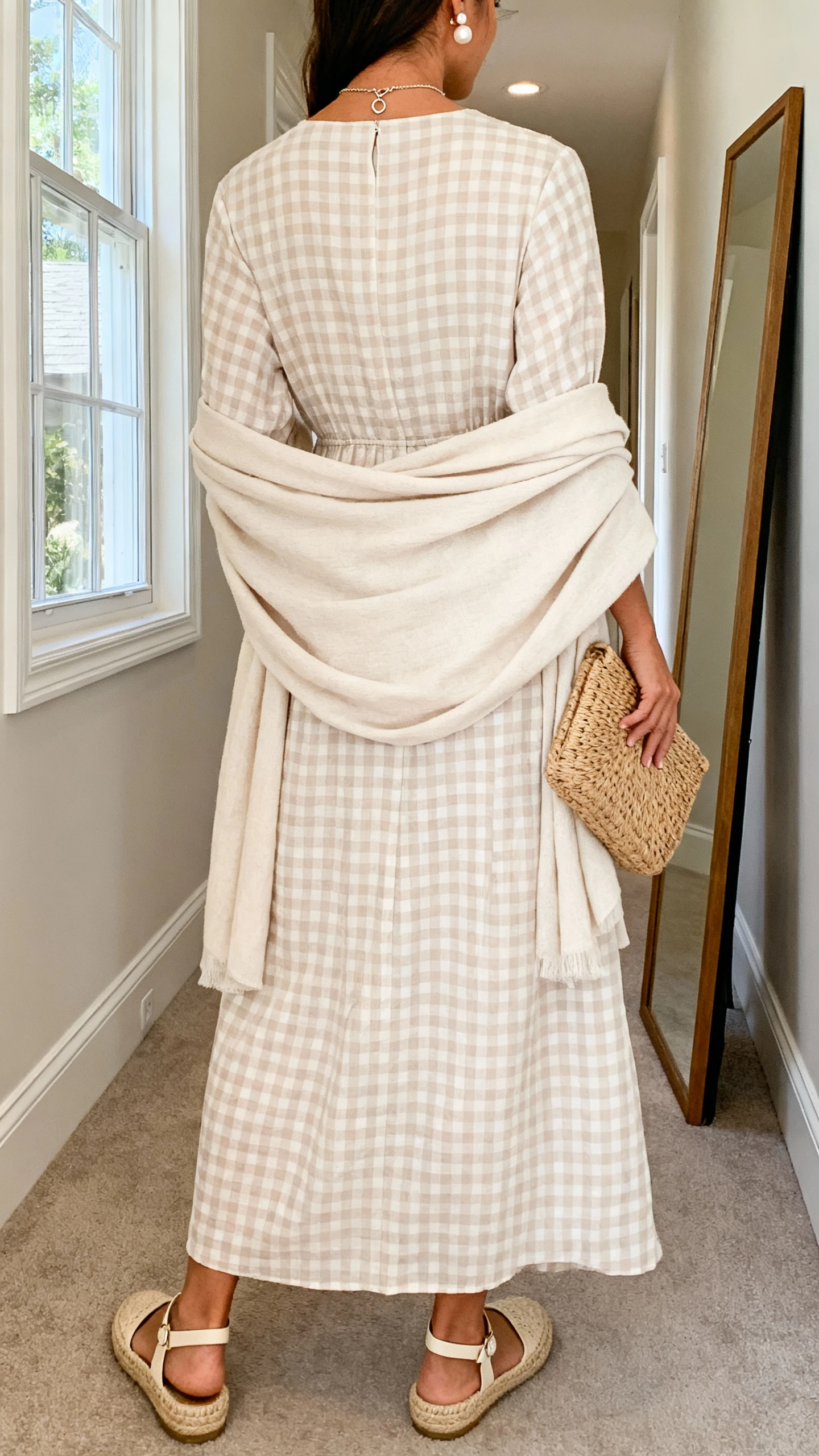 iPhone back-view photo of a woman wearing a tone-on-tone check maxi dress (cream-on-cream or sand-on-sand), a soft matching wrap, ankle-strap flats or low espadrilles in natural tones, pearl studs, a dainty pendant necklace, and a woven clutch; face not visible, hallway full-length mirror, gentle window light, iPhone photo quality.