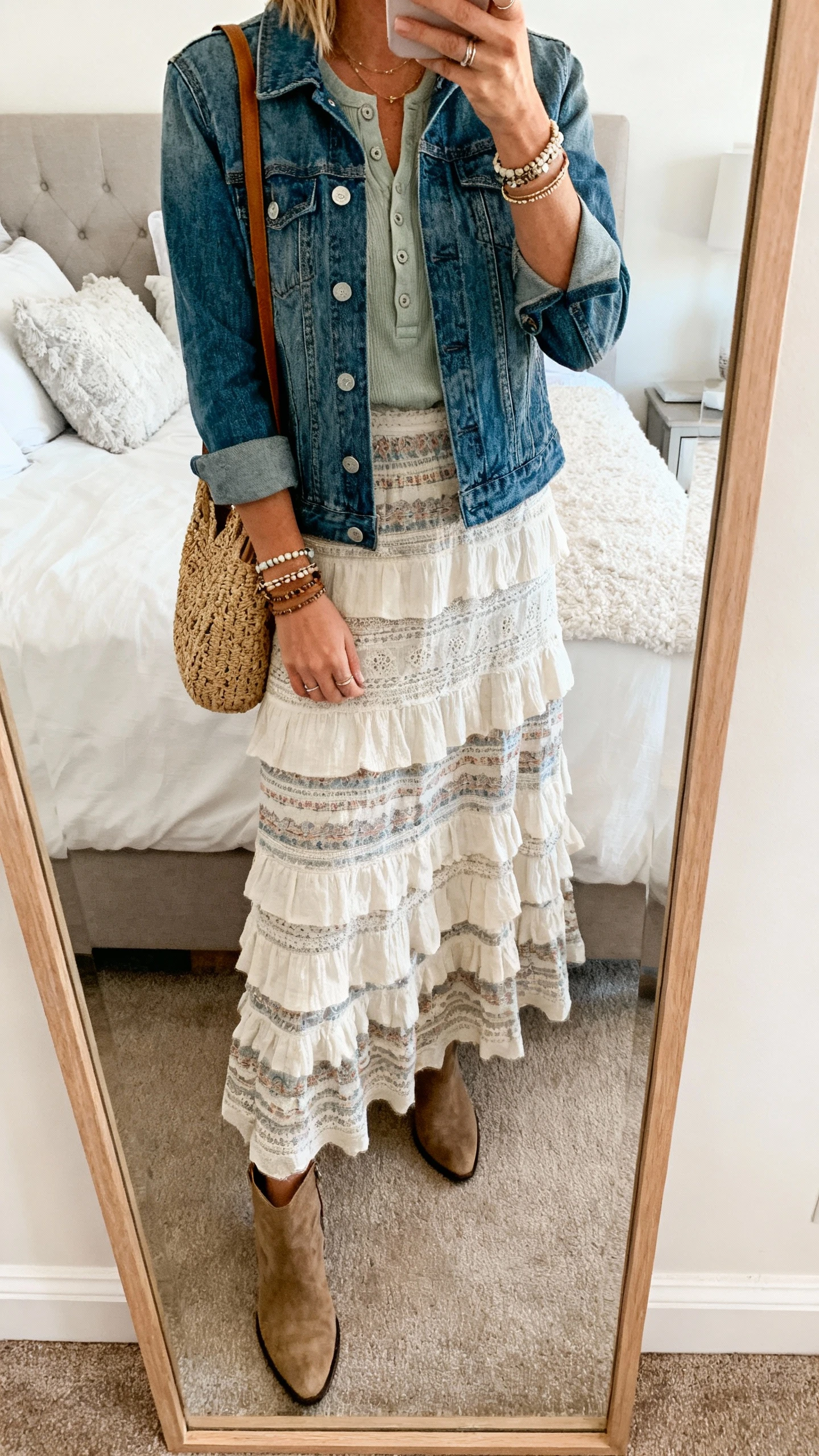 iPhone mirror selfie of a woman wearing a boho tiered maxi skirt, classic denim jacket over a tucked henley, ankle boots, layered bracelets, and a woven tote, face not visible, cropped at shoulders, bedroom mirror, soft daylight, iPhone photo quality.