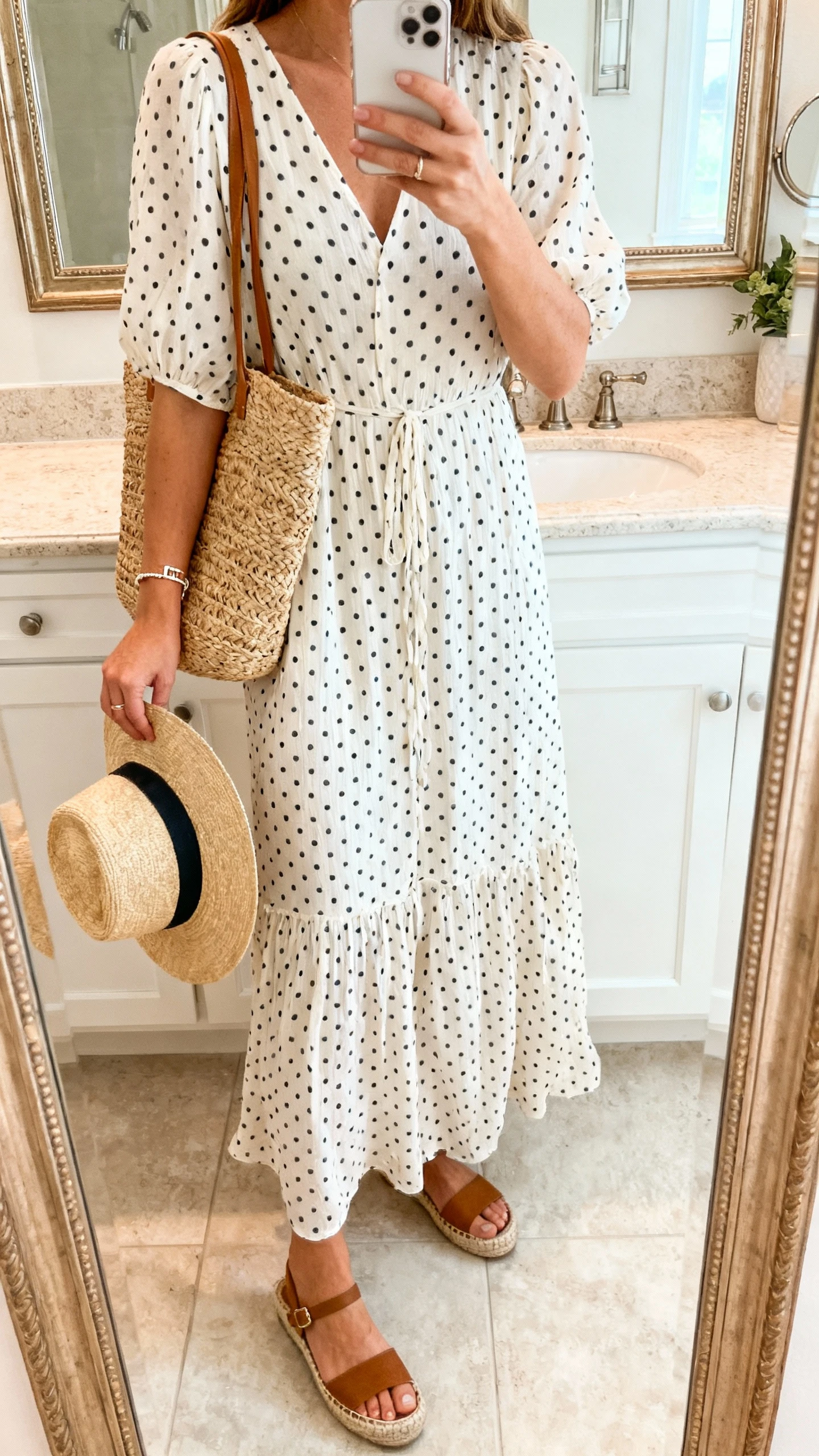 iPhone mirror selfie of a woman wearing a breezy polka dot maxi dress with espadrille wedges, straw tote bag, sun hat in hand, dainty bracelet, face not visible, cropped at shoulders, bathroom mirror with bright natural light, iPhone photo quality