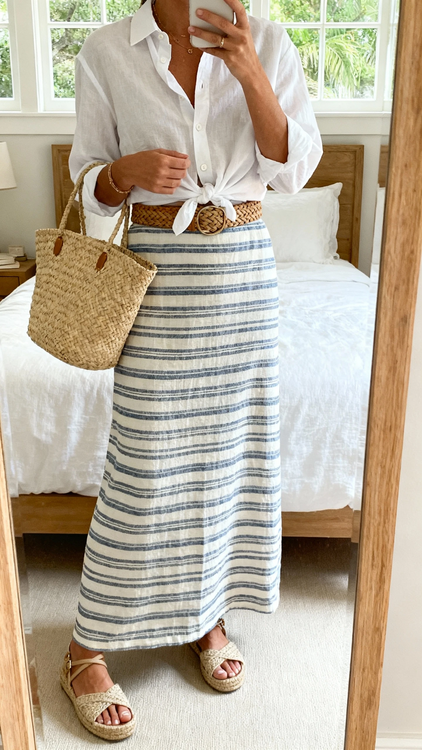 iPhone mirror selfie of a woman wearing a coastal-cool striped maxi skirt with a crisp white button-down half-tucked, woven belt, espadrille sandals, raffia tote, face not visible, cropped at shoulders, bedroom mirror, soft window light, iPhone photo quality.