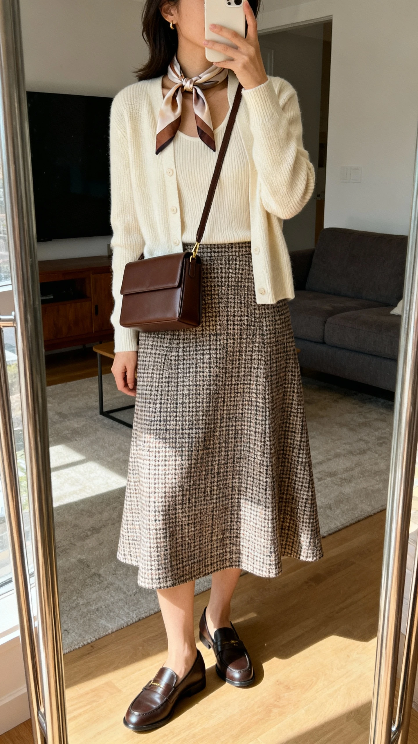 iPhone mirror selfie of a woman wearing a houndstooth midi A-line skirt, a cream fine-knit shell, a matching cardigan, sleek loafers, a boxy espresso crossbody bag, and a silk neck scarf in subtle complementary tones, face not visible, side angle, living room full-length mirror, indoor daylight, iPhone photo quality.