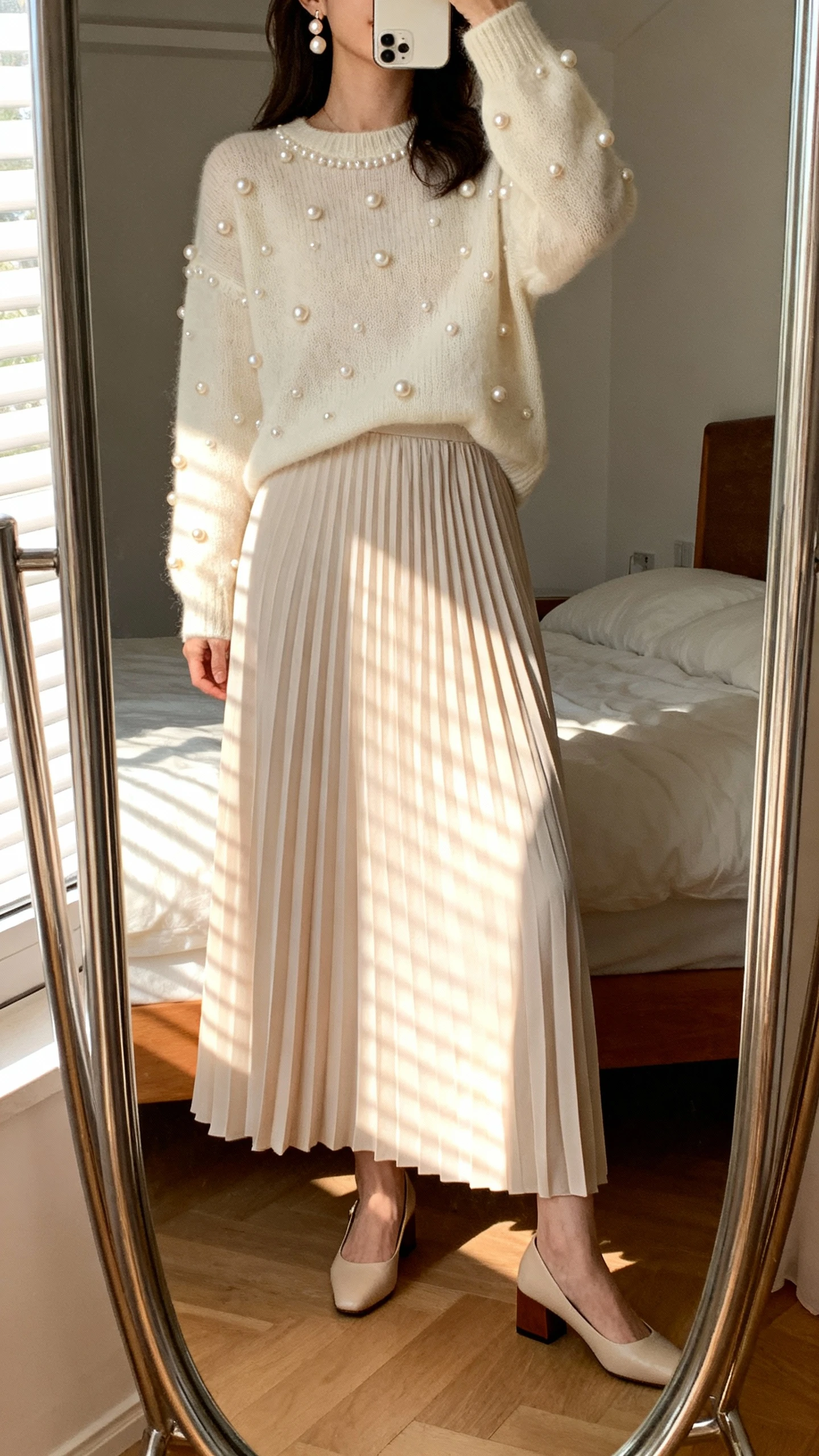 iPhone mirror selfie of a woman wearing a long soft-pleated maxi skirt, a pearl-embellished sweater, delicate pearl earrings, and low block-heel pumps, face not visible, cropped at neck, bedroom mirror with morning window light, iPhone photo quality.