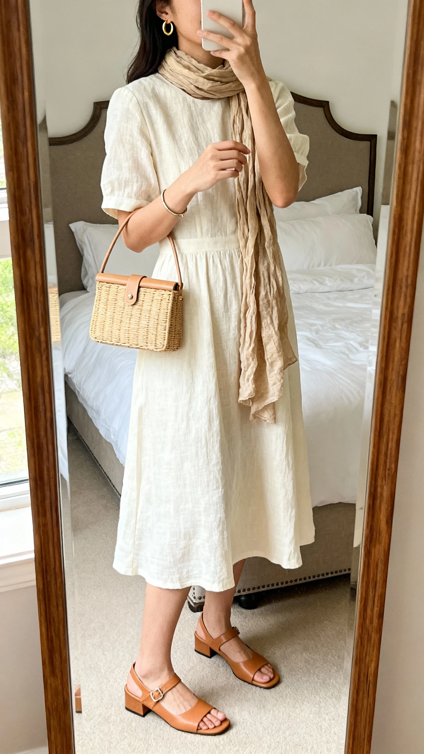 iPhone mirror selfie of a woman wearing a midi-length linen A-line dress in cream with low block-heel leather sandals in camel, delicate gold hoop earrings, a slim bracelet, a structured mini tote in natural, and a lightweight matching linen-blend scarf, face not visible, cropped at neck, bedroom mirror with natural morning light, iPhone photo quality.