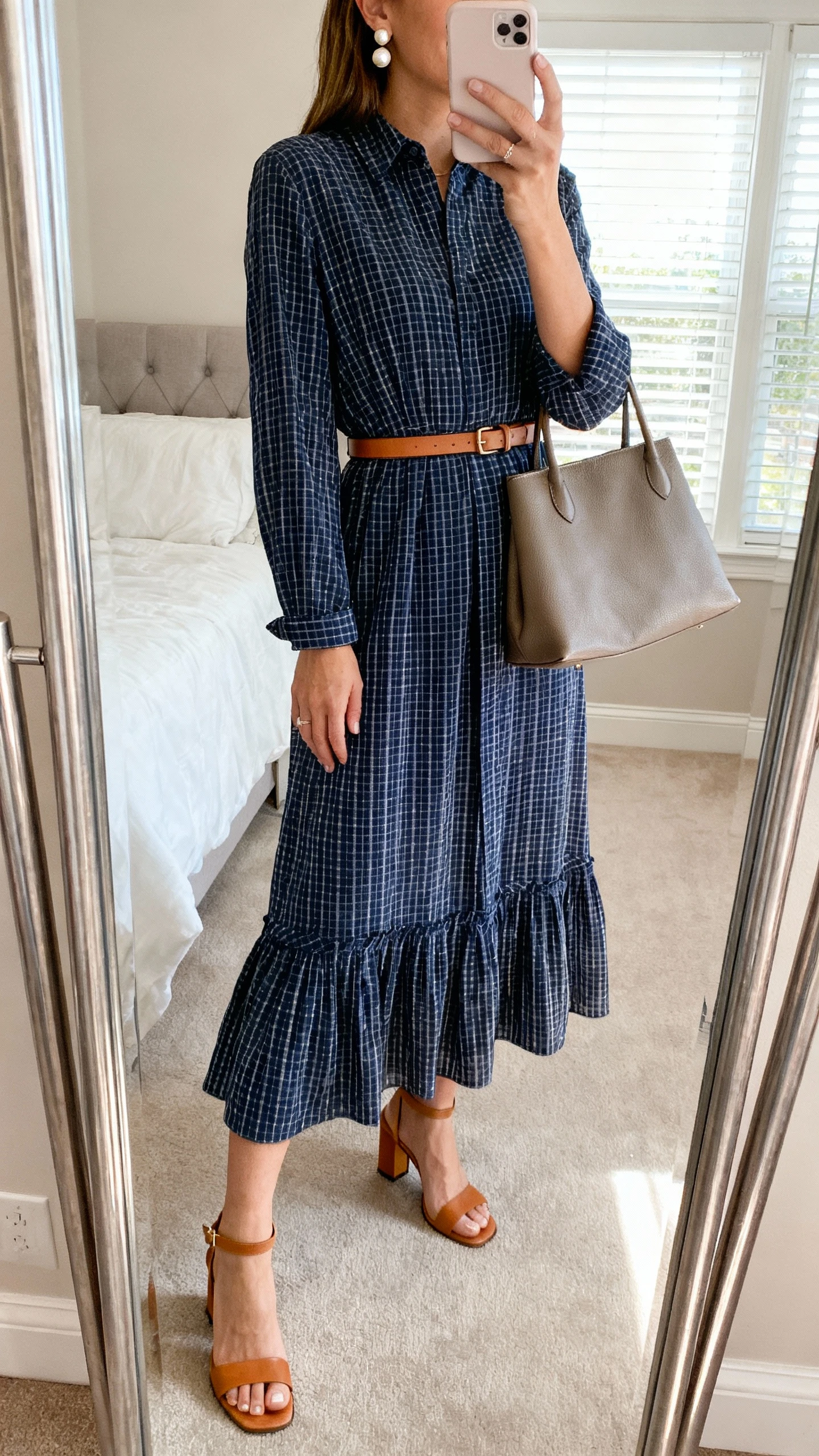 iPhone mirror selfie of a woman wearing a navy gingham belted maxi dress with a subtle tiered hem, paired with tan heeled sandals, a slim leather belt, pearl stud earrings, and a structured tote, face not visible, bedroom full-length mirror, soft window light, iPhone photo quality.