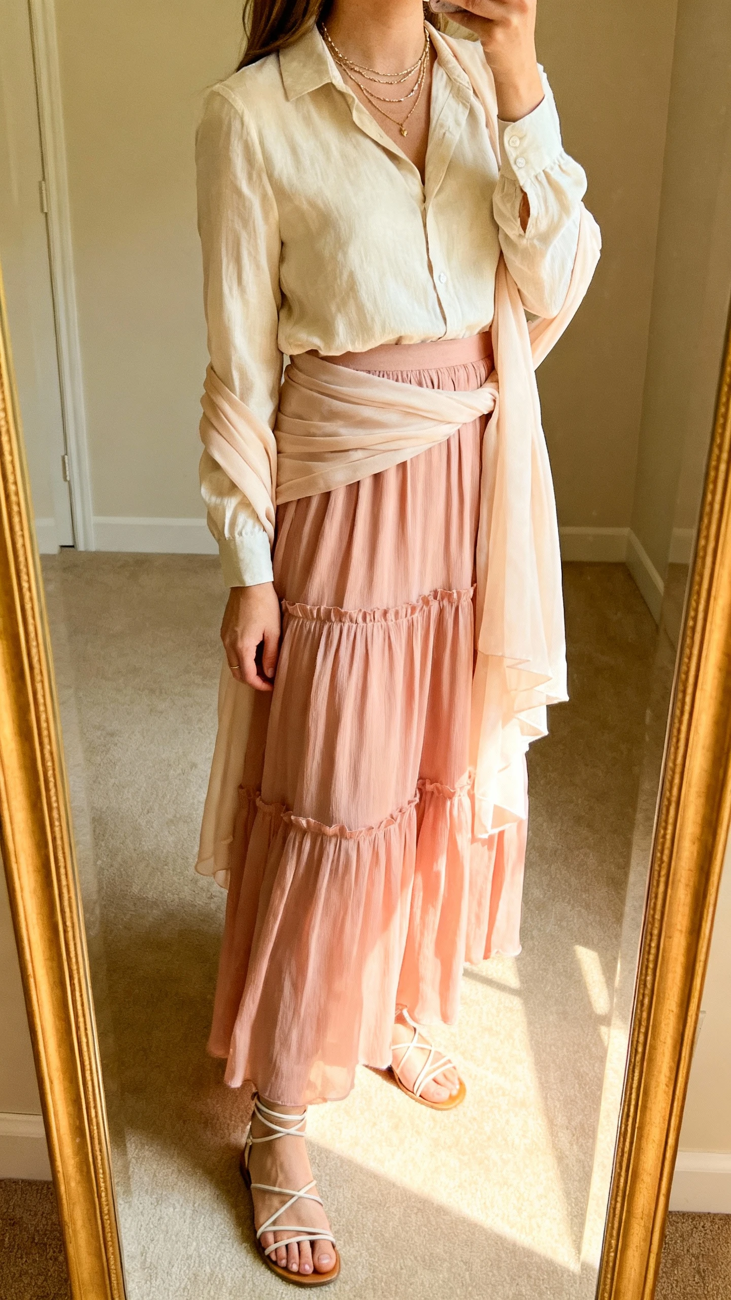 iPhone mirror selfie of a woman wearing a romantic flowy maxi skirt in blush with a lightweight blouse tucked in, chiffon wrap or duster layer, dainty layered necklaces, and strappy sandals, face not visible, side angle, full-length mirror in softly lit room, iPhone photo quality