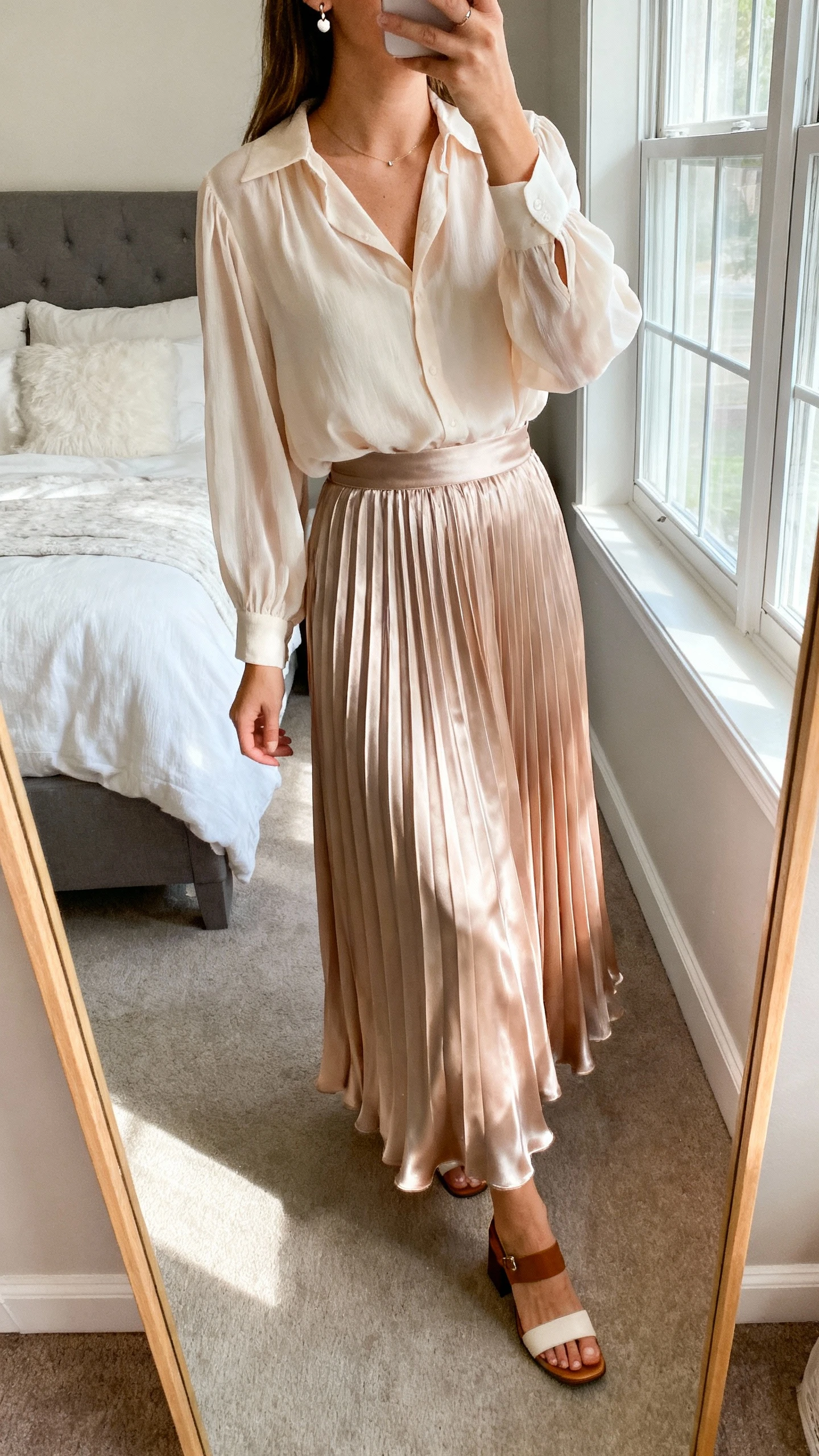 iPhone mirror selfie of a woman wearing a soft chiffon blouse tucked into a pleated satin maxi skirt that floats with every step, paired with delicate stud earrings and low block-heel sandals, face not visible, cropped at neck, bedroom mirror, natural window light, iPhone photo quality.