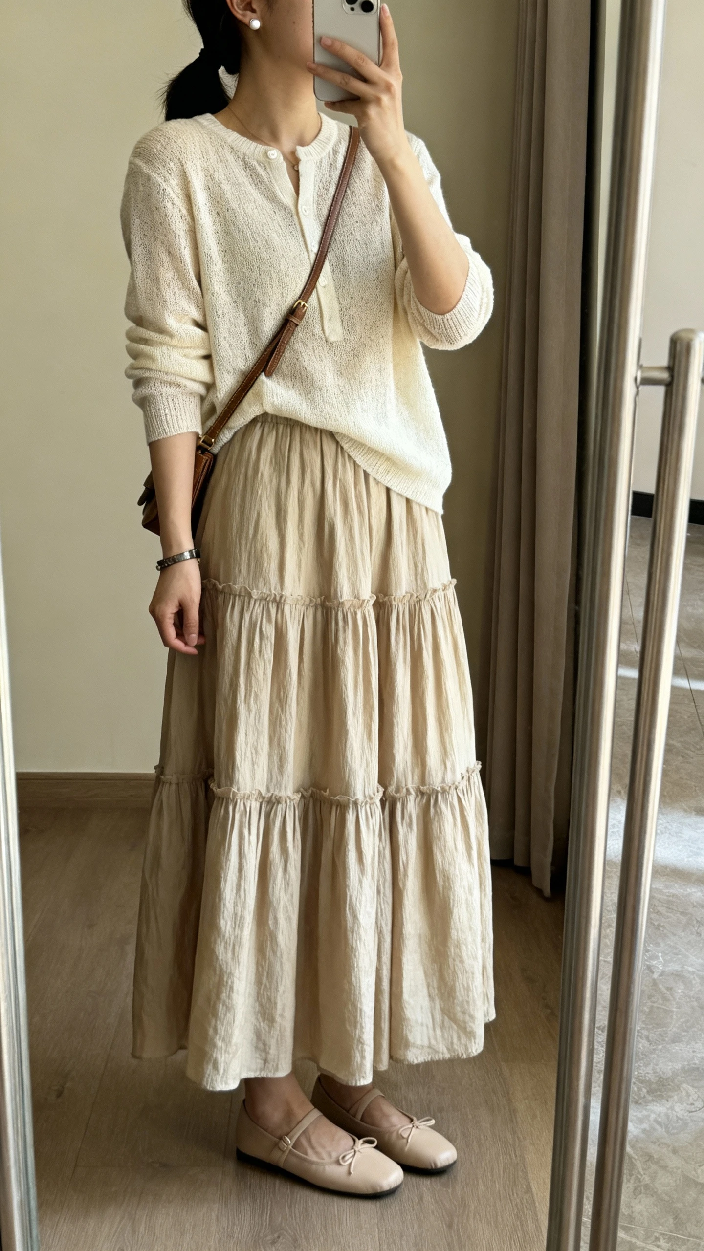 iPhone mirror selfie of a woman wearing a soft knit blouse with a tiered maxi skirt, ballet flats, a crossbody bag, simple bracelet, and stud earrings, face not visible, side angle in a full-length mirror, warm indoor lighting, iPhone photo quality.