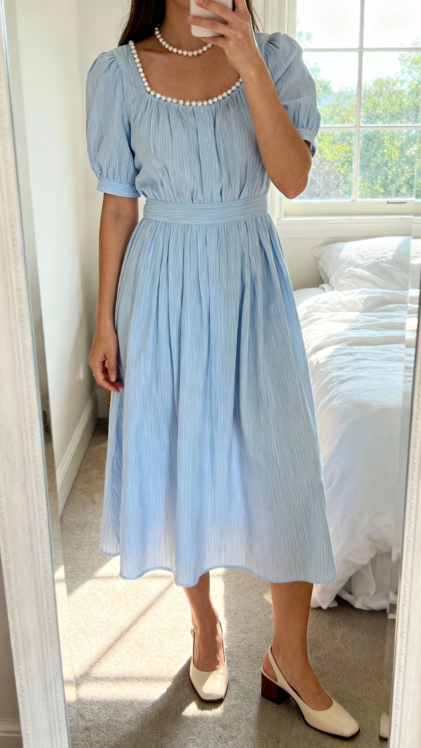 iPhone mirror selfie of a woman wearing a soft sky-blue striped cotton midi dress with delicate pearls and low block heels, face not visible, cropped at neck, bedroom mirror with morning window light, iPhone photo quality.