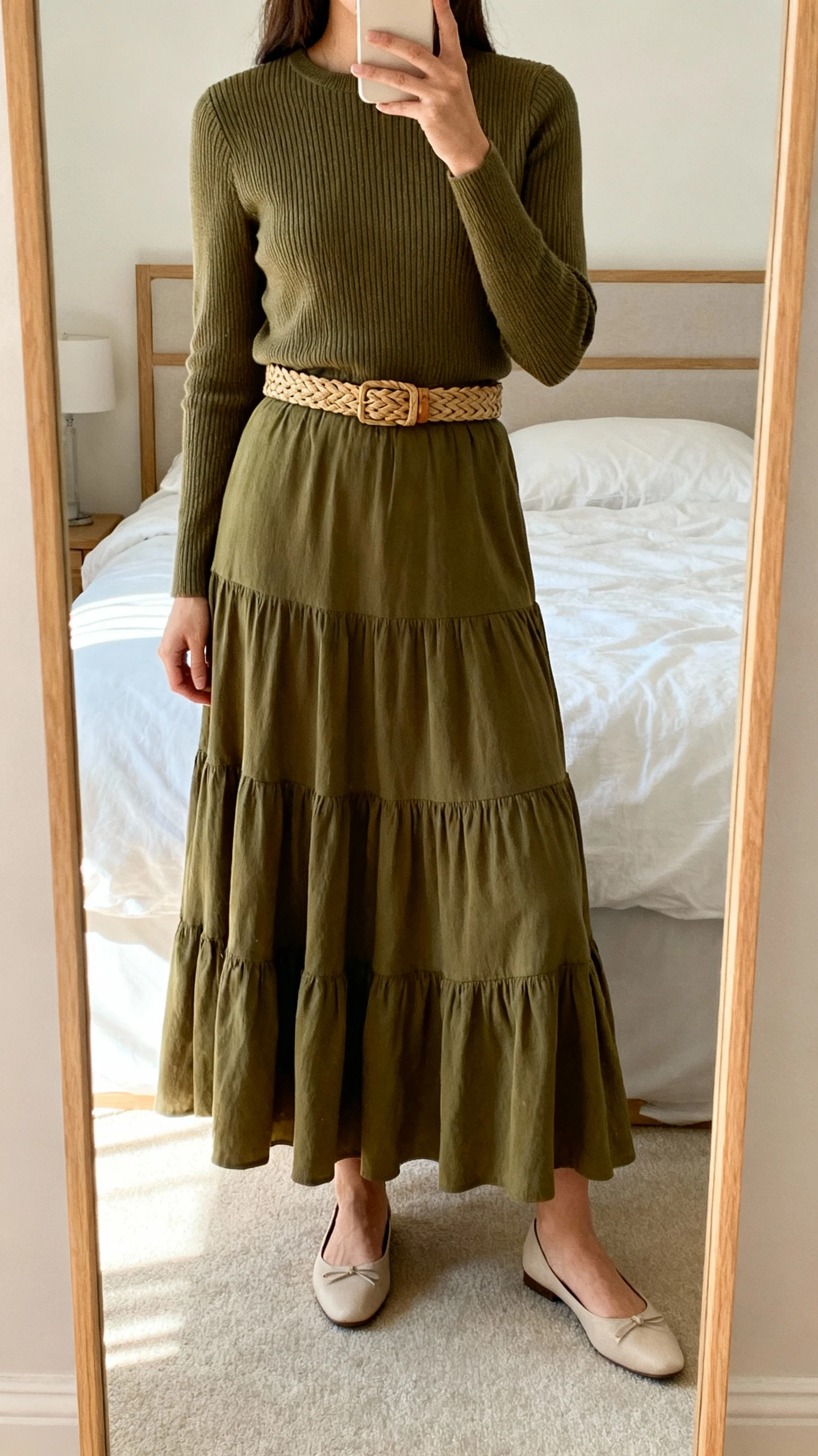 iPhone mirror selfie of a woman wearing a tiered maxi skirt in olive with a tailored knit top, classic flats, and an optional woven belt defining the waist; face not visible, cropped at shoulders, bedroom mirror, soft afternoon light, iPhone photo quality.
