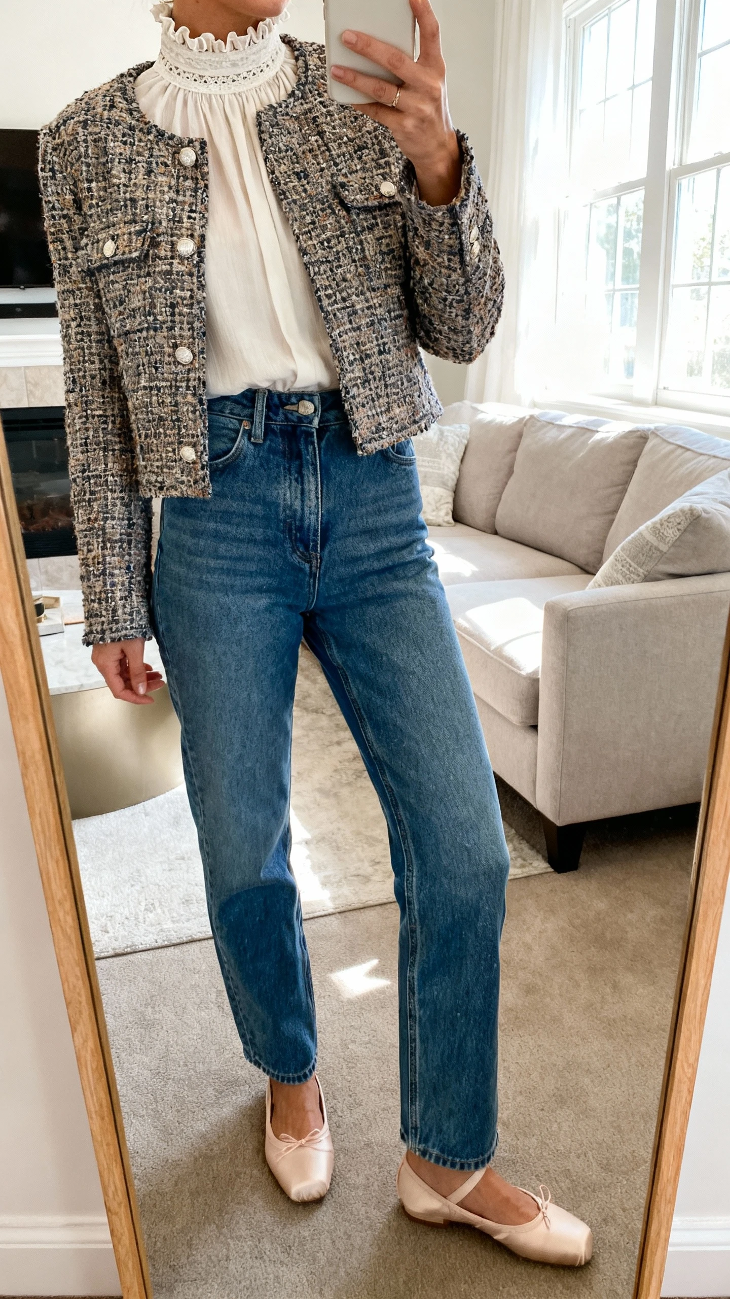 iPhone mirror selfie of a woman wearing high-rise straight-leg jeans with no distressing, a graceful high-neck blouse with subtle ruffles or lace trim, a cropped tweed jacket, and refined ballet flats, face not visible, cropped at neck, living room mirror, bright window light, iPhone photo quality.