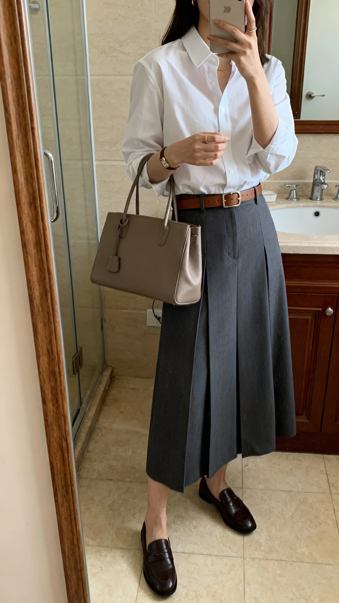 iPhone mirror selfie side angle of a woman wearing a crisp classic button-down shirt with an A-line maxi skirt, leather belt, structured tote, and loafers, face not visible, bathroom full-length mirror, morning indoor light, iPhone photo quality.