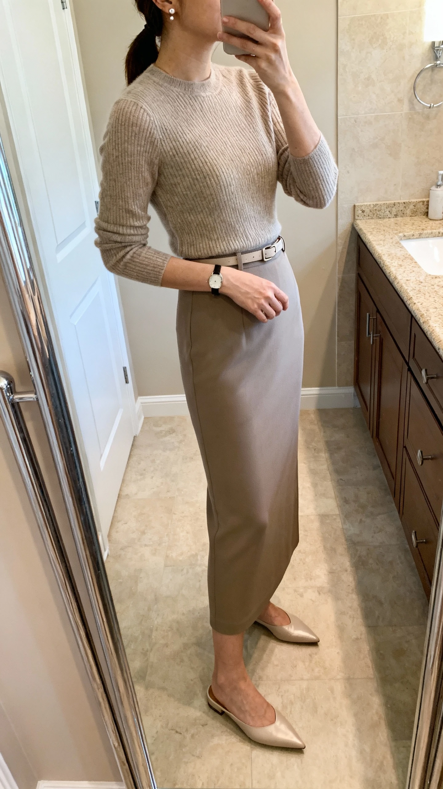 iPhone side-angle mirror selfie of a woman wearing a sleek column skirt with a fine-knit fitted sweater, minimal belt, pointed-toe flats, delicate stud earrings, slim wristwatch, face not visible, bathroom full-length mirror, soft indoor lighting, iPhone photo quality
