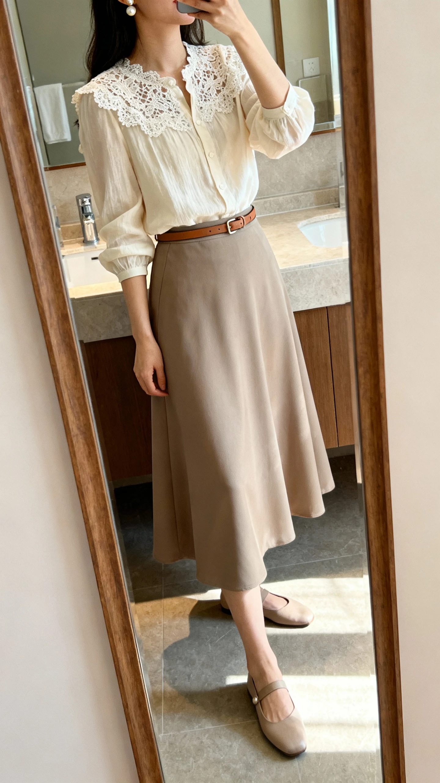 iPhone side-angle mirror selfie of a woman wearing a lace-trim blouse with an A-line maxi skirt for classic grace, styled with a thin leather belt, pearl studs, and simple flats, face not visible, bathroom full-length mirror, morning light, iPhone photo quality.