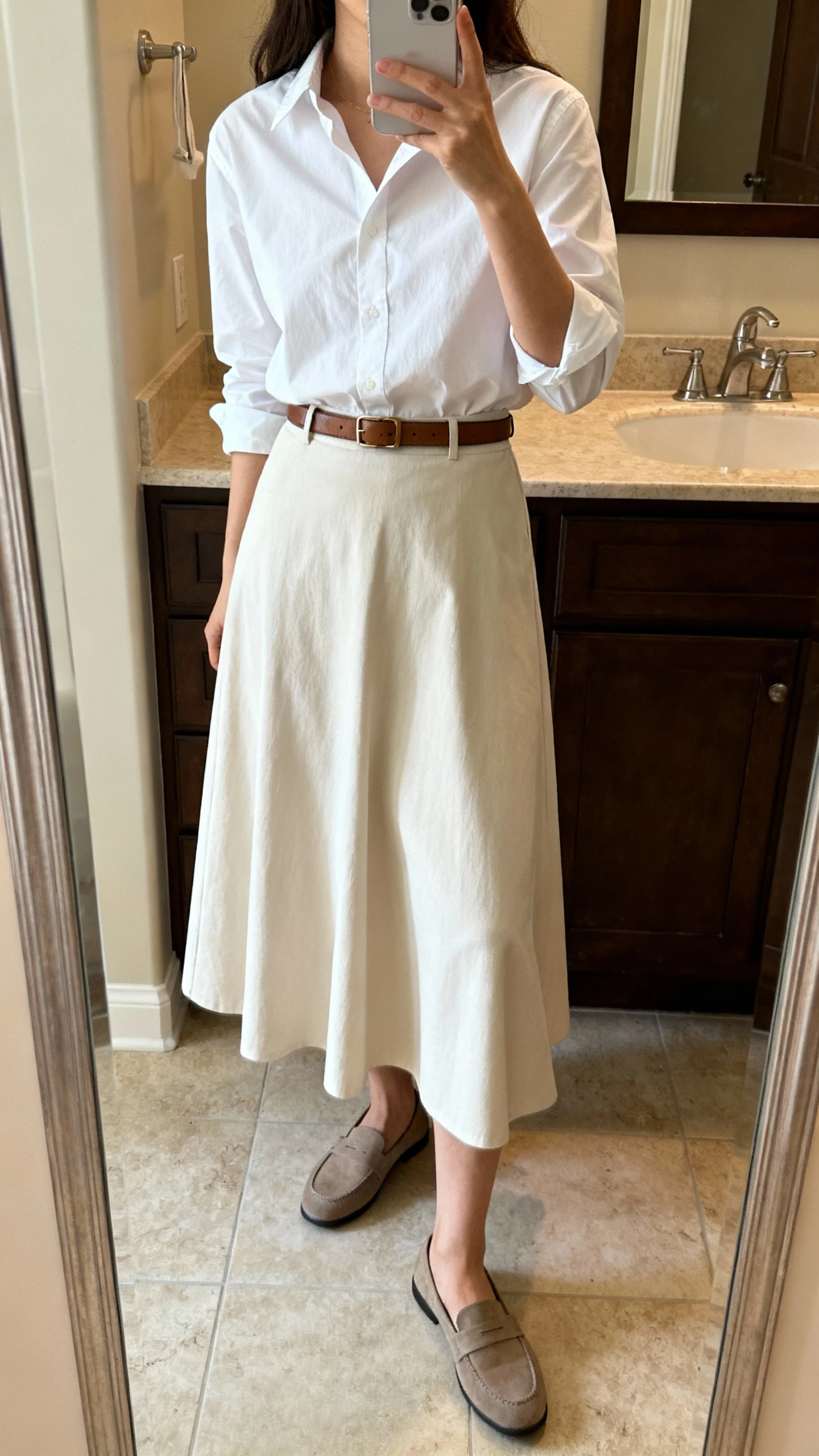 iPhone side-angle mirror selfie of a woman wearing a crisp white classic oxford blouse tucked into an A-line maxi skirt with a slim leather belt and simple loafers, face not visible, bathroom full-length mirror, indoor lighting, iPhone photo quality.